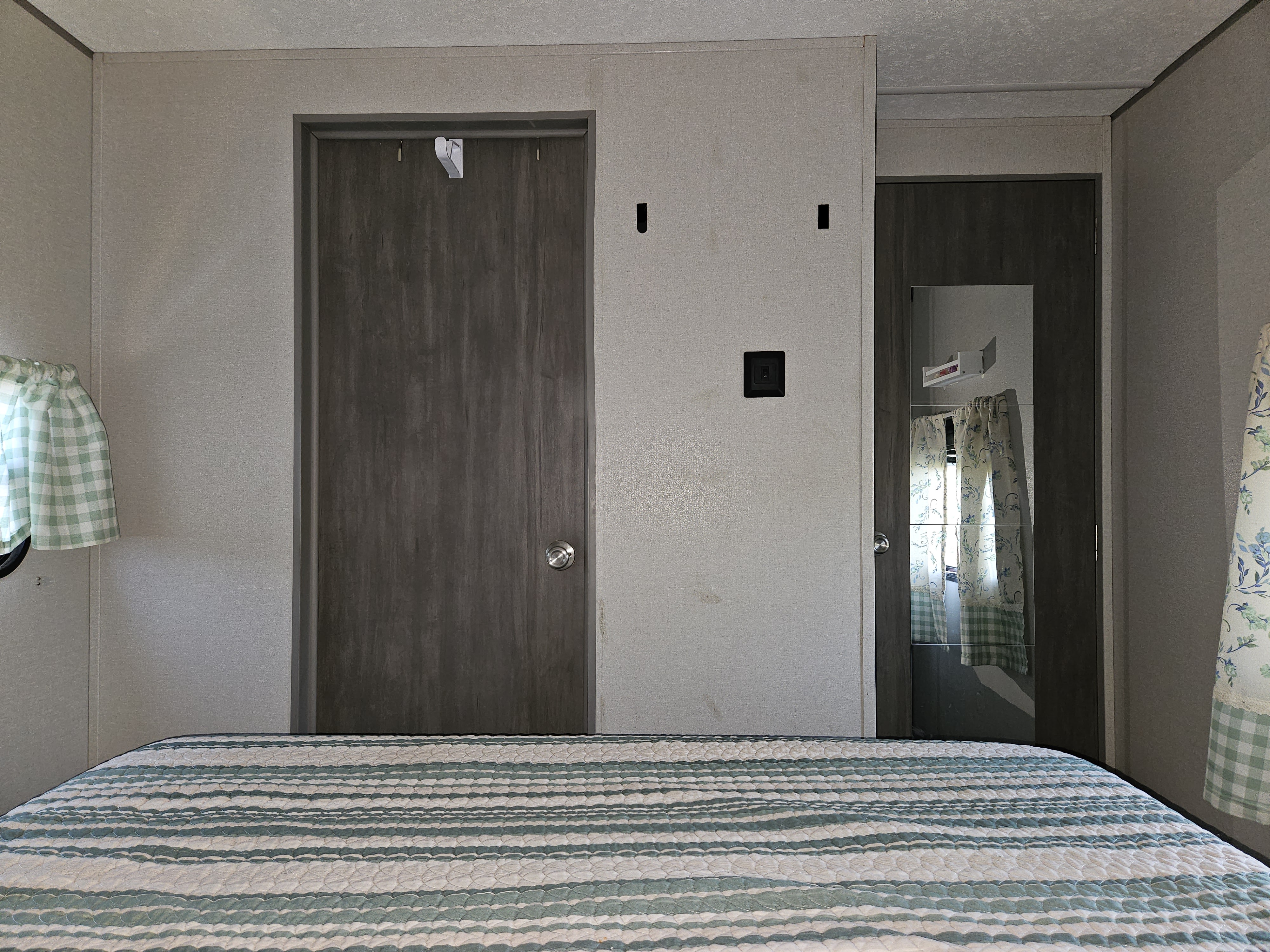 Compact RV rental bedroom featuring a striped bed, two doors, and patterned curtains. Cozy travel space.. Coachmen Catalina Legacy 2024