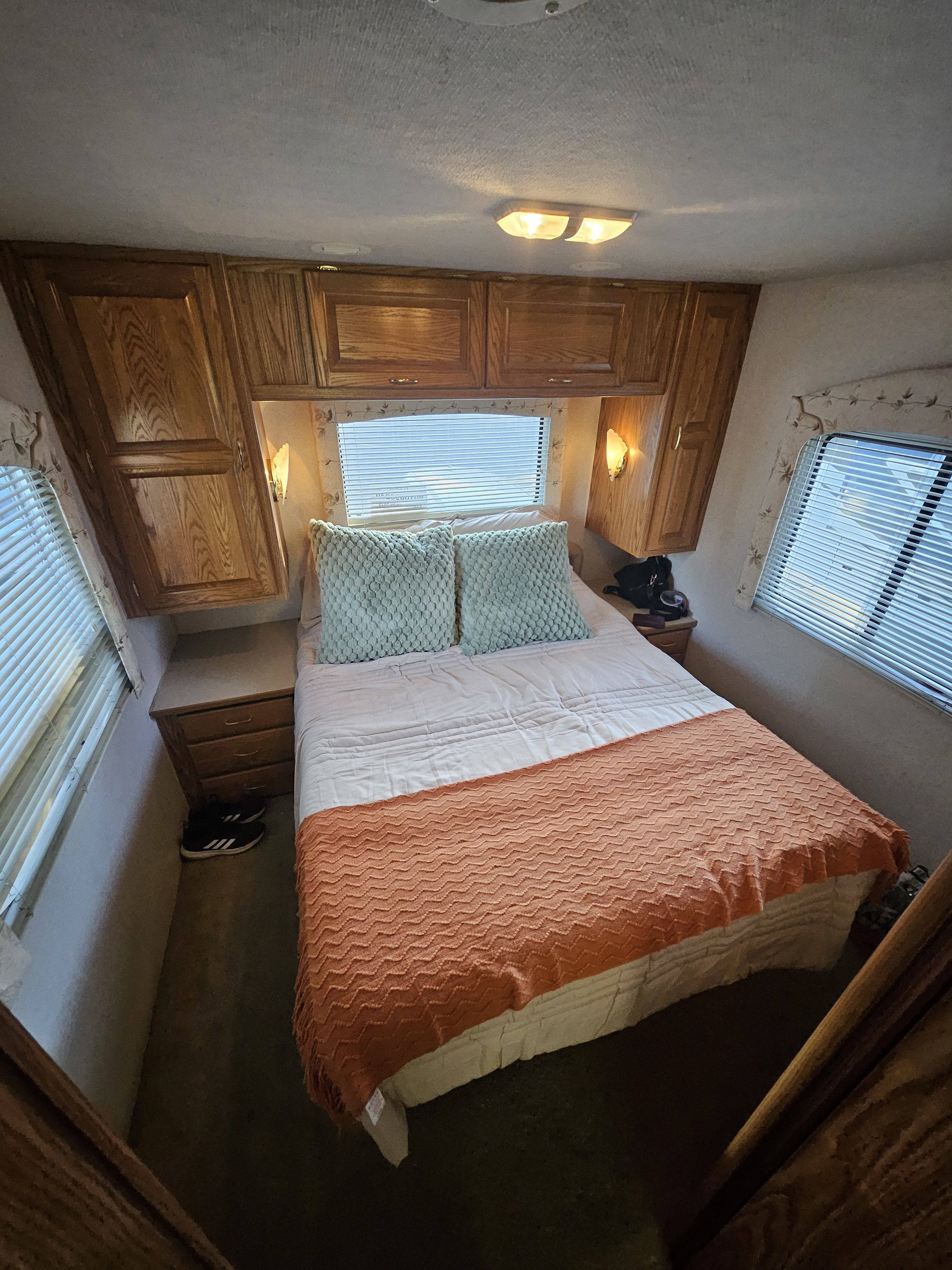 Cozy RV rental bedroom with wooden cabinets, windows, and a bed featuring light blue pillows and an orange blanket.. Sea Breeze SB300 2002