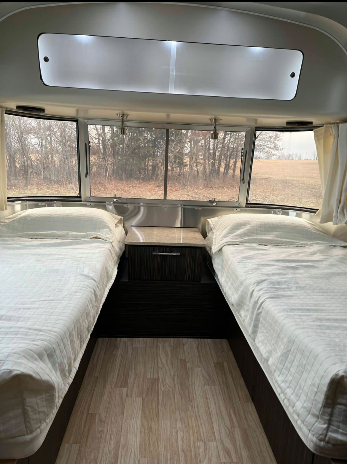 Inside an RV rental: a spacious bedroom with two twin beds, a central cabinet, and large windows offering scenic views.. Airstream International 2016
