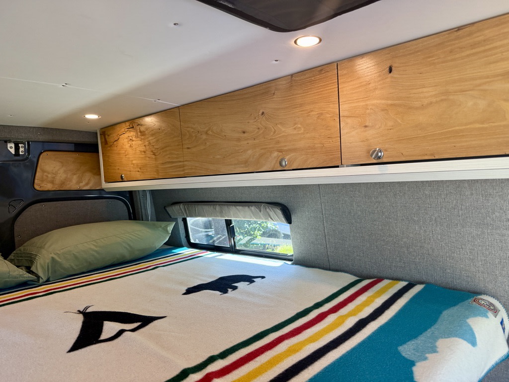 Cozy camper van RV rental with a comfy bed, illuminated wood cabinets, and a colorful striped blanket, ideal for travel.. Mercedes Sprinter 170 4X4 2018