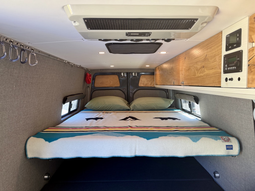 Cozy RV rental interior featuring a comfortable bed, overhead storage, and climate controls. Perfect for adventure!. Mercedes Sprinter 170 4X4 2018