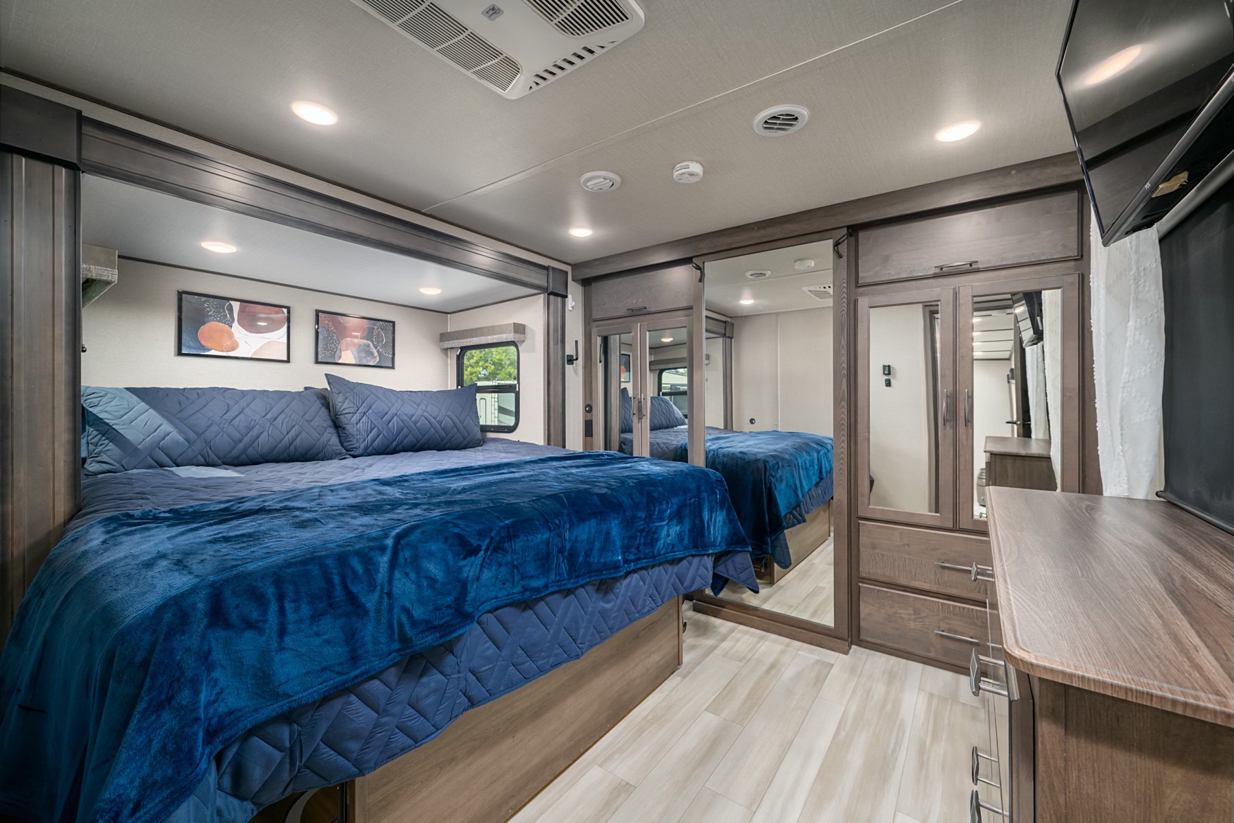 Spacious RV rental bedroom featuring a large bed with blue bedding, built-in mirrored wardrobe, and dresser.. Grand Design Solitude 2022