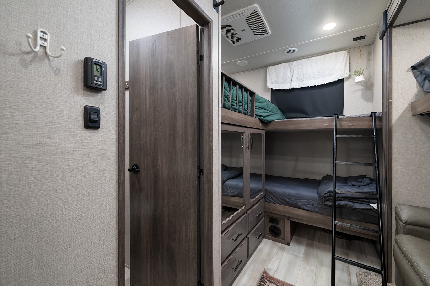 RV rental interior showcasing space-saving bunk beds, a ladder, and built-in storage. Ideal for travel, with controls on the wall.. Grand Design Solitude 2022