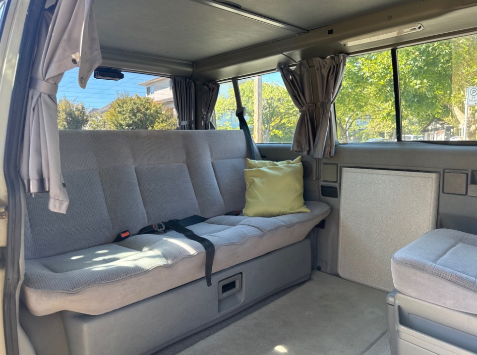 Inside this RV rental: a cozy bench seat with seatbelts, tied-back curtains, and a built-in storage/fridge area.. Volkswagen T4 Westfalia 1993