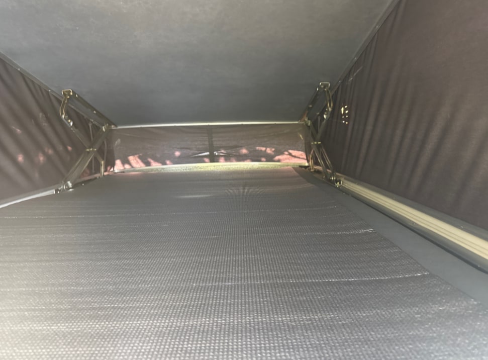 Interior view of an RV rental's pop-top sleeping area, featuring a dark, textured mattress and lift mechanism.. Volkswagen T4 Westfalia 1993