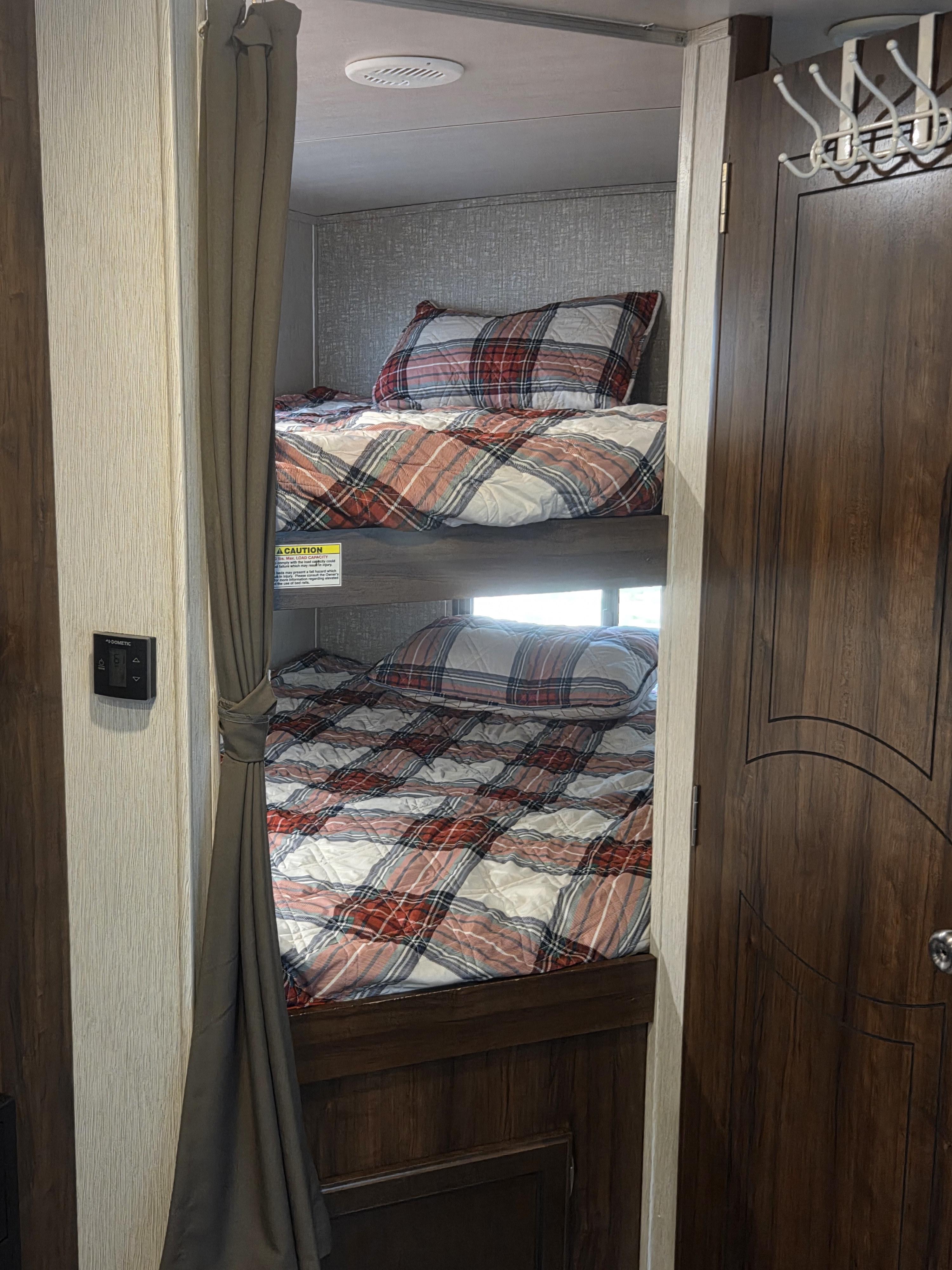 Cozy RV rental interior showcasing comfortable bunk beds with plaid bedding and a Dometic control panel.. Heartland RVs Mallard 2018