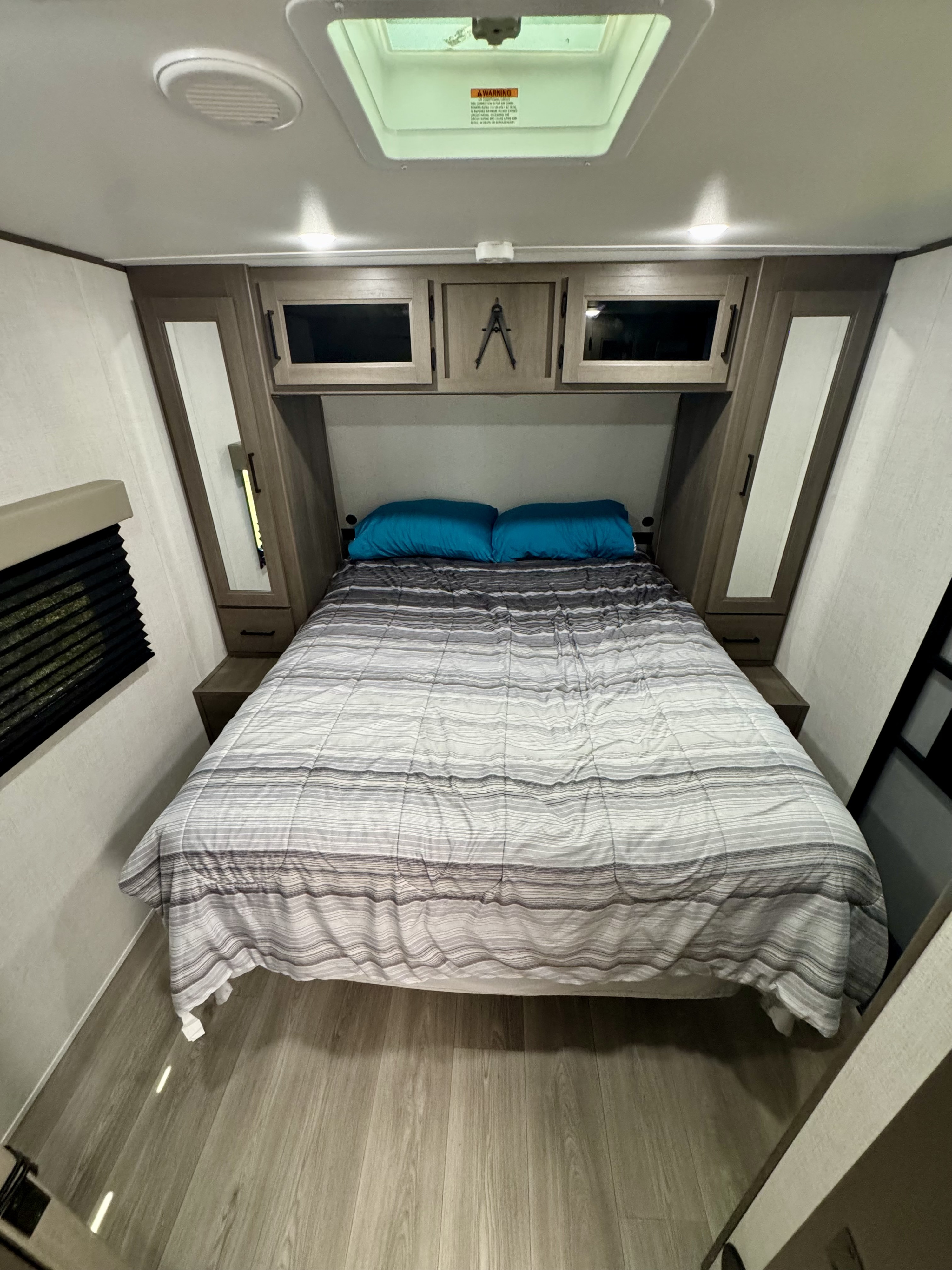 Comfortable RV rental bedroom featuring a striped bed, overhead storage, side cabinets, and a ceiling skylight.. Grand Design Transcend 245RLT 2025