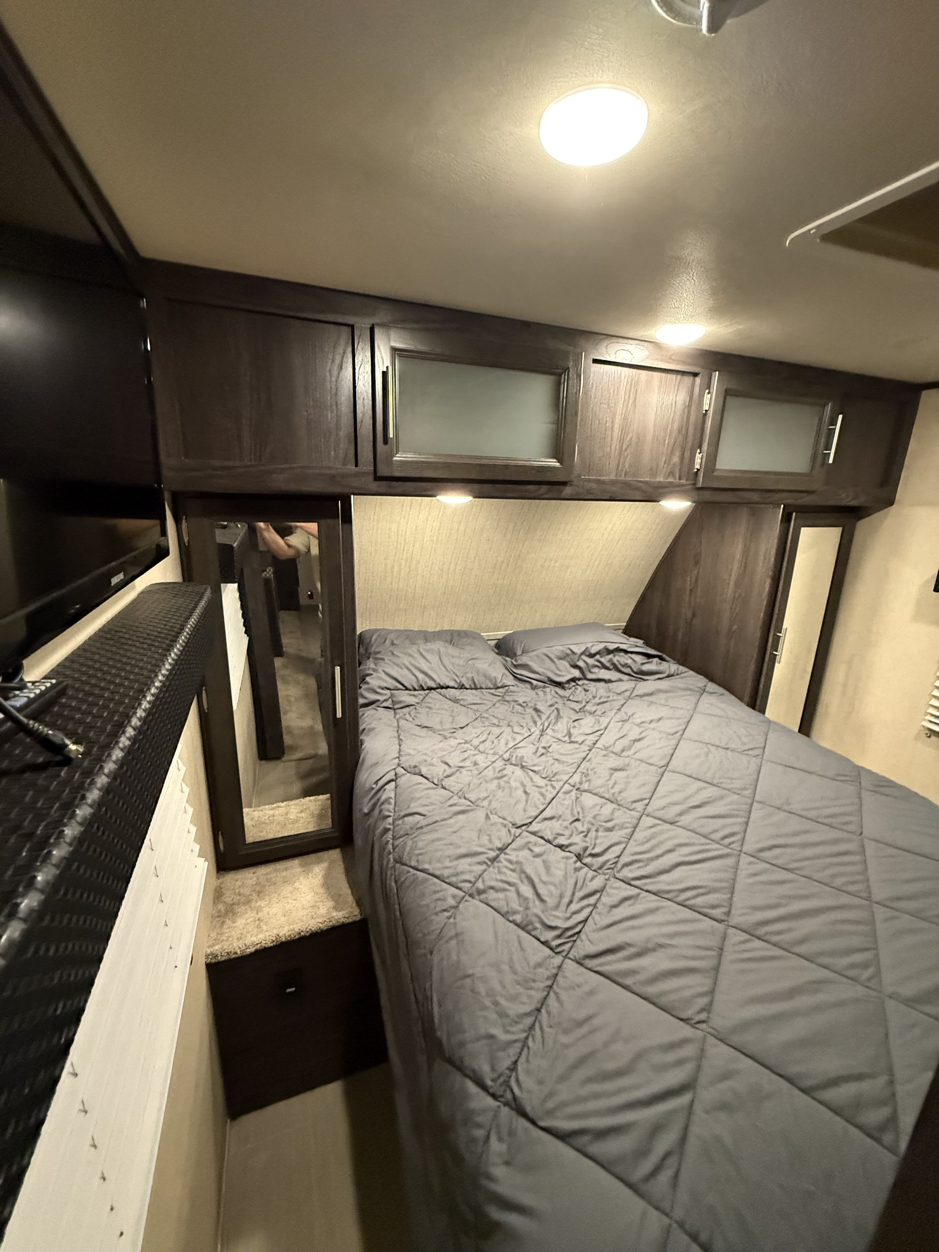 Comfortable RV rental bedroom featuring a comfy bed, dark wood cabinets, TV, and mirror. Brightly lit for your stay.. Dutchmen Kodiak Ultimate 2018