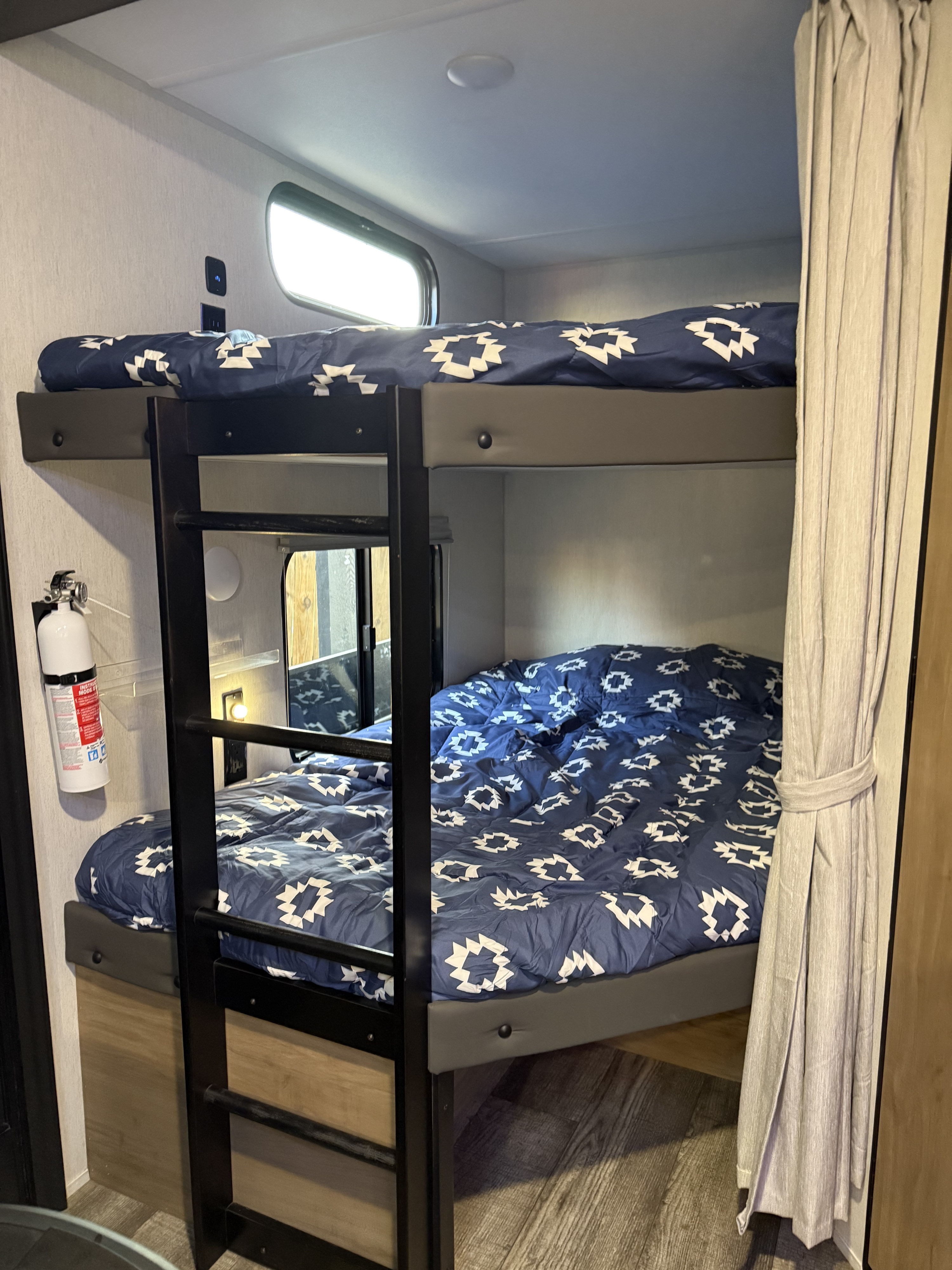 Bunk beds in a clean RV rental, featuring blue patterned comforters, a ladder, and safety essentials for a comfortable camper interior.. Forest River Cherokee 2023