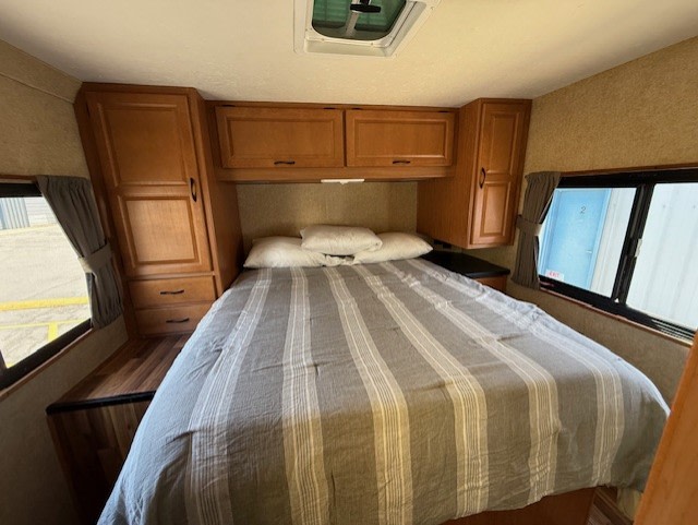 Cozy RV rental bedroom with striped bedding, ample wood storage cabinets, and bright windows on both sides.. Thor Majestic 2016