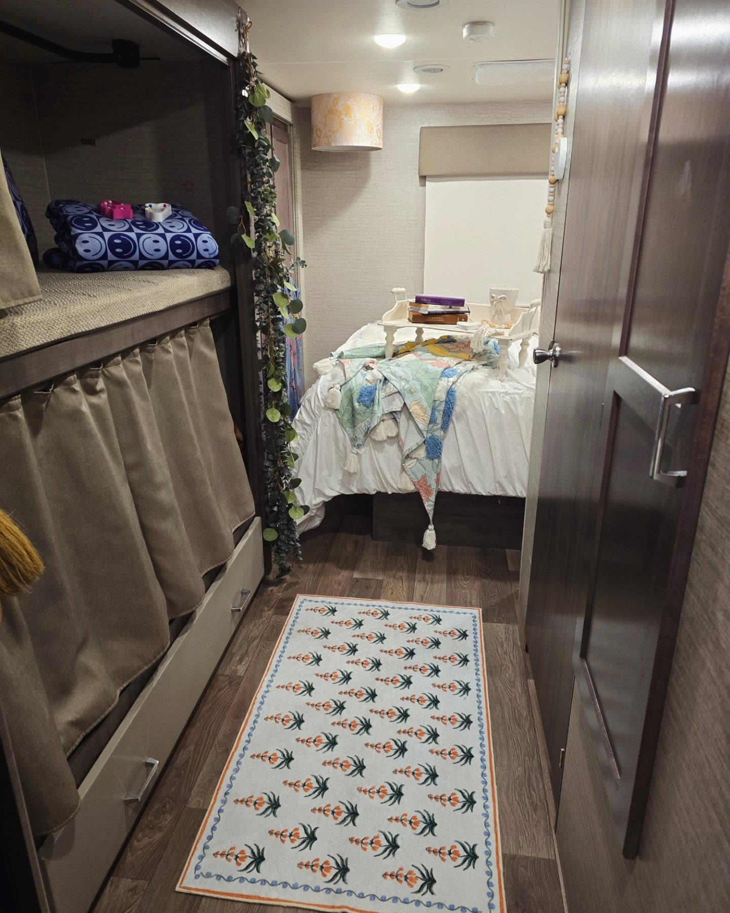 This inviting RV rental interior features a cozy bunk area, main bed with books, and a patterned rug on wood floors.. Winnebago Spirit 2024