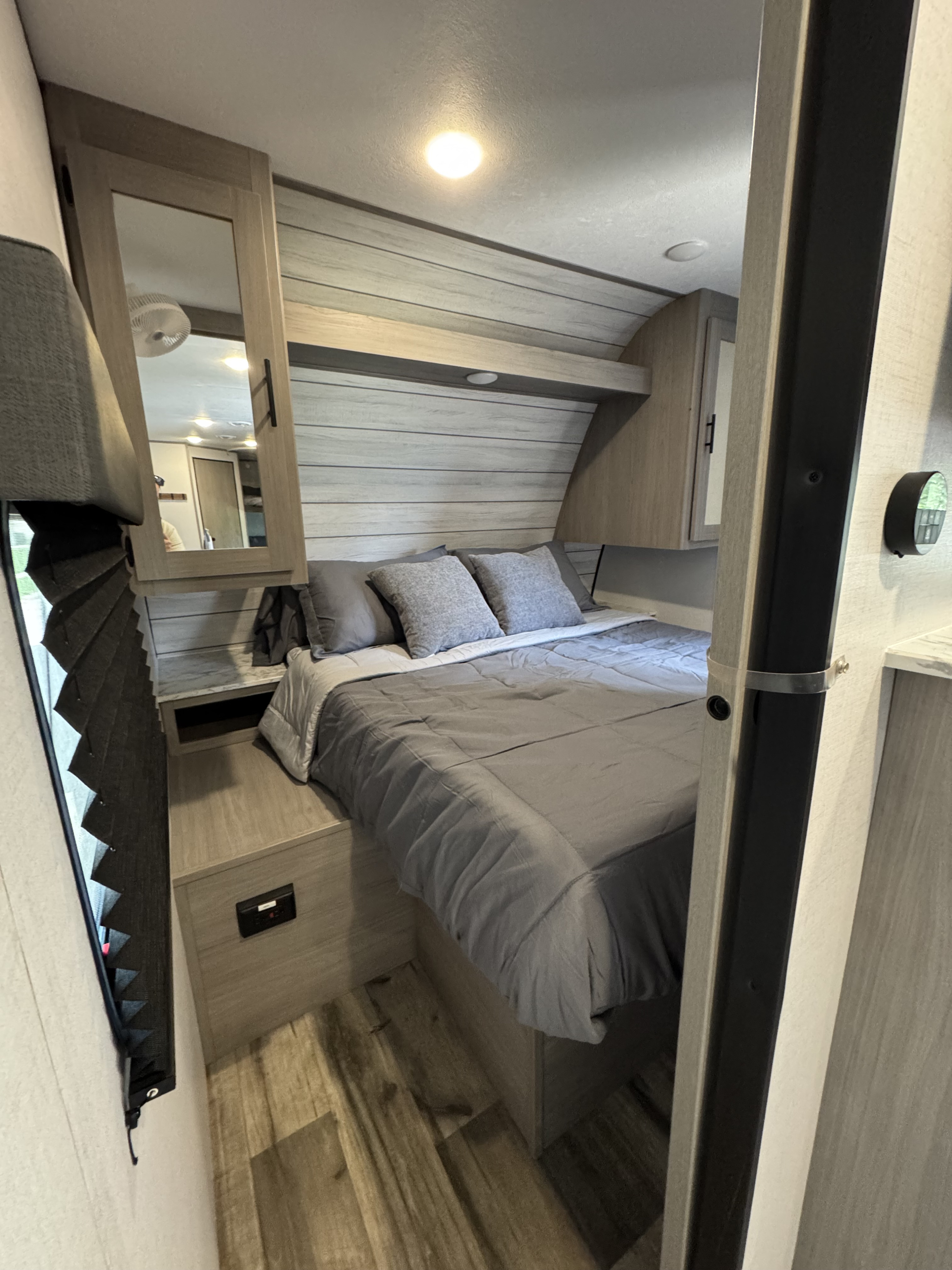Compact RV rental bedroom with a gray bed, wood-paneled walls, mirrored cabinet, and window blind for comfortable travel.. Dutchmen Coleman lantern 262BH 2024