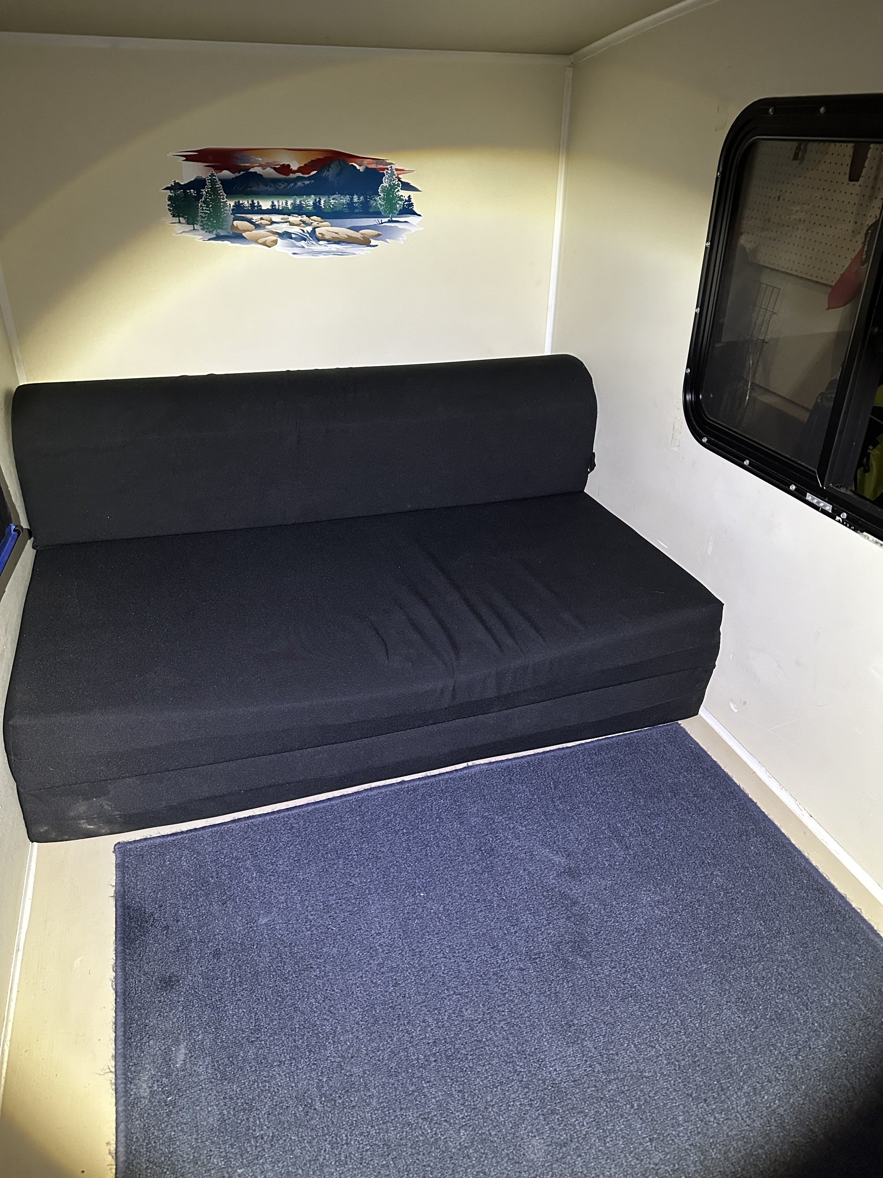 Inside this RV rental: a black sofa bed along the back wall, a blue rug on the floor, and a nature decal above the sofa.. Runaway Coolcamp 2021
