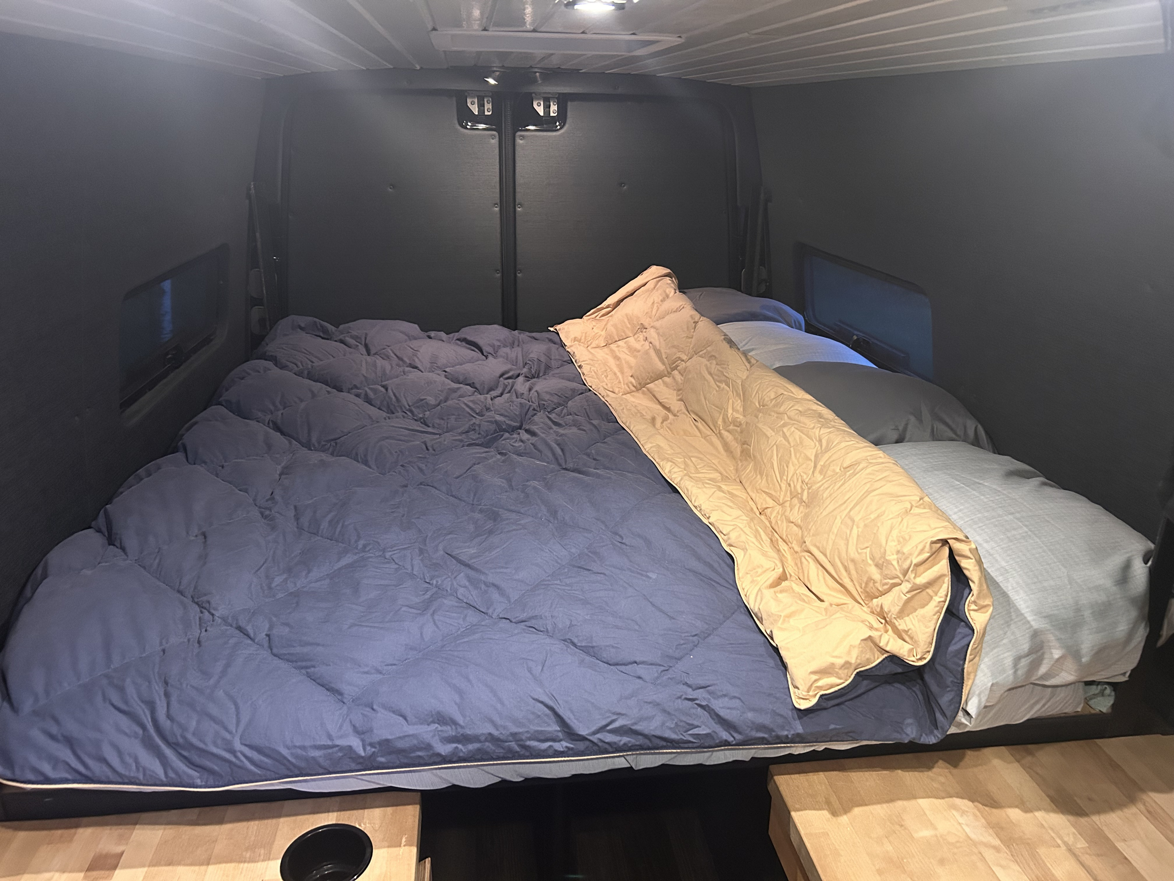 Comfortable RV rental bed setup, with blue comforter, pillows, and a tan sleeping bag in a cozy interior.. Mercedes Sprinter 2013