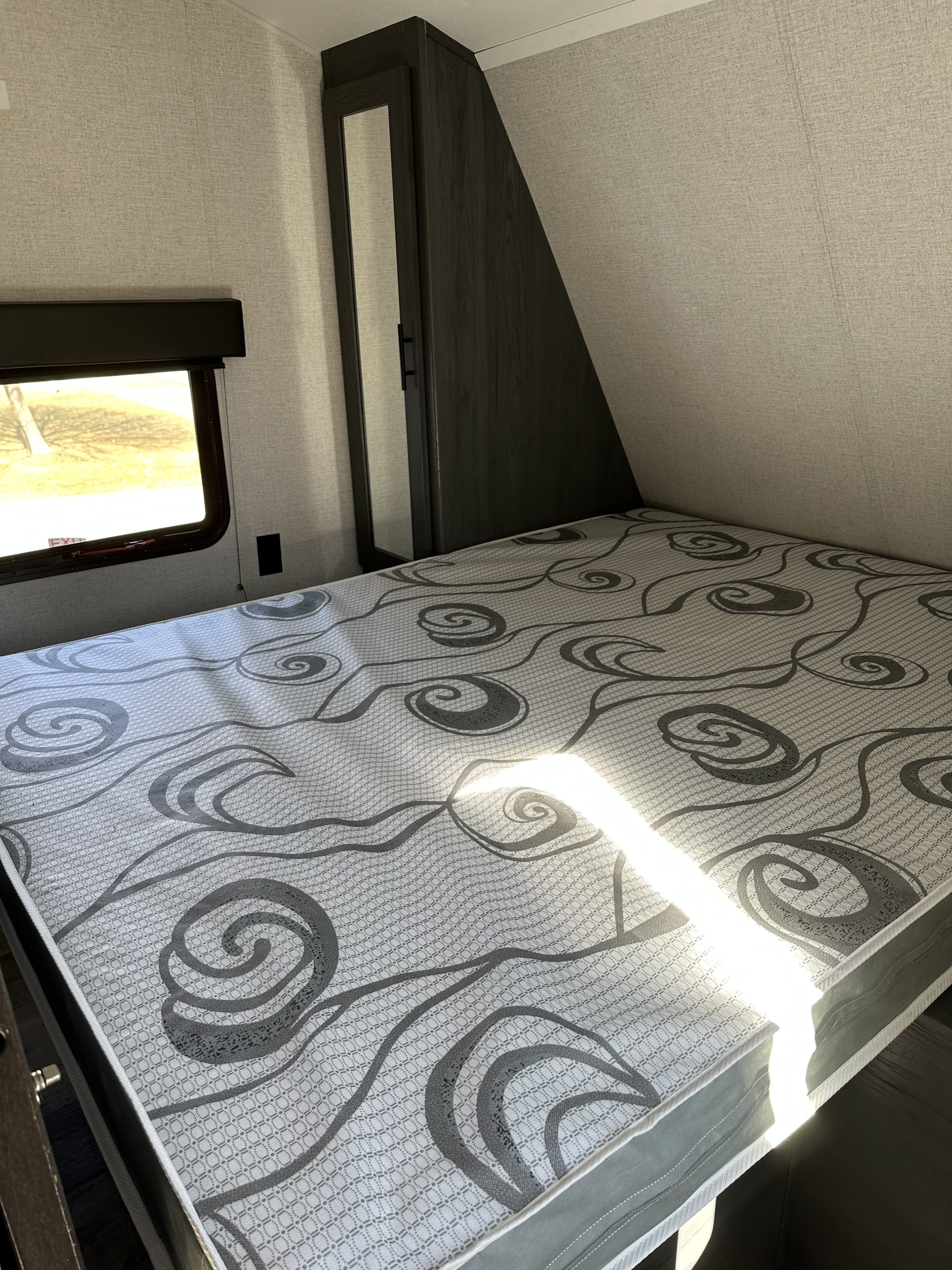 RV rental interior: bedroom with patterned mattress, side window, and mirrored cabinet. Ready for travel adventures.. Dutchmen Aspen Trail LE 29BH 2021