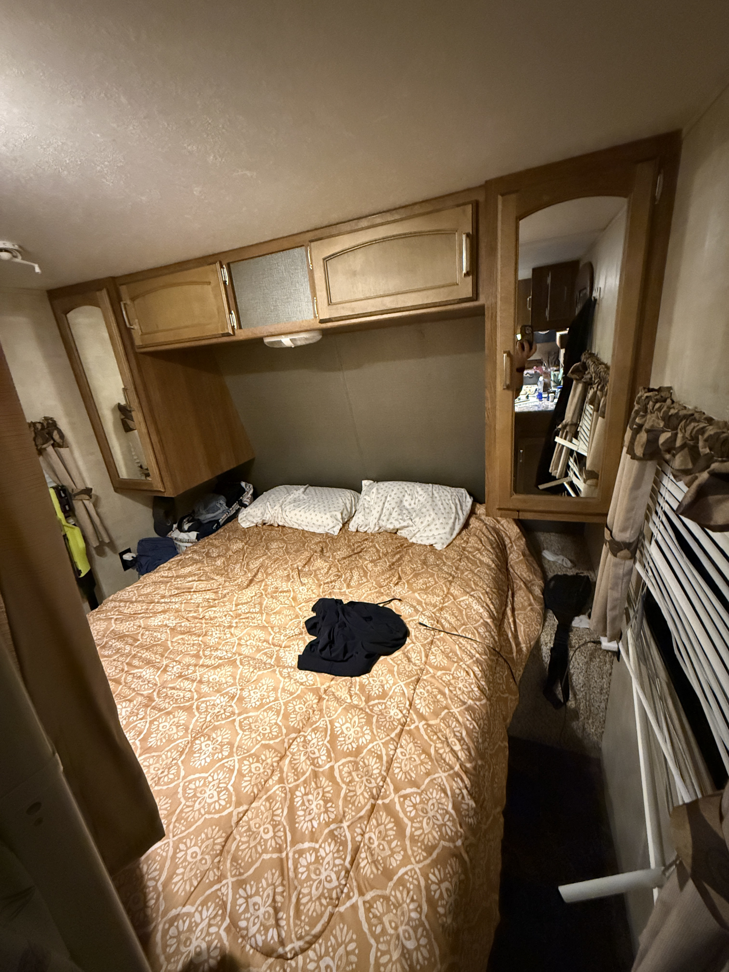 Cozy RV rental bedroom featuring a patterned bed, overhead cabinets, and a mirror reflecting the interior.. Keystone RV Springdale 2014