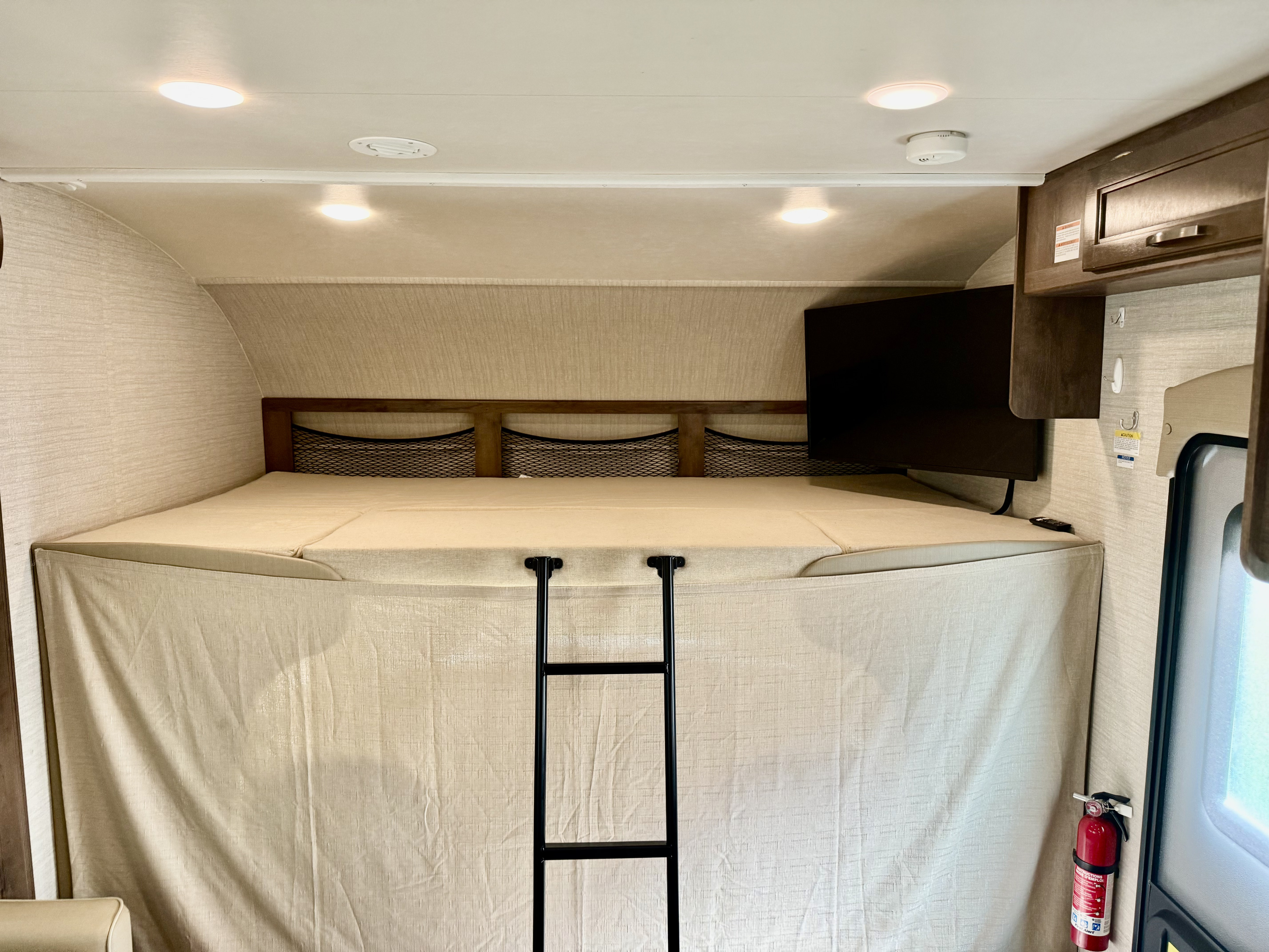 The cab-over bunk bed area of an RV rental, complete with a ladder, TV, and essential safety features.. Jayco Redhawk 2020