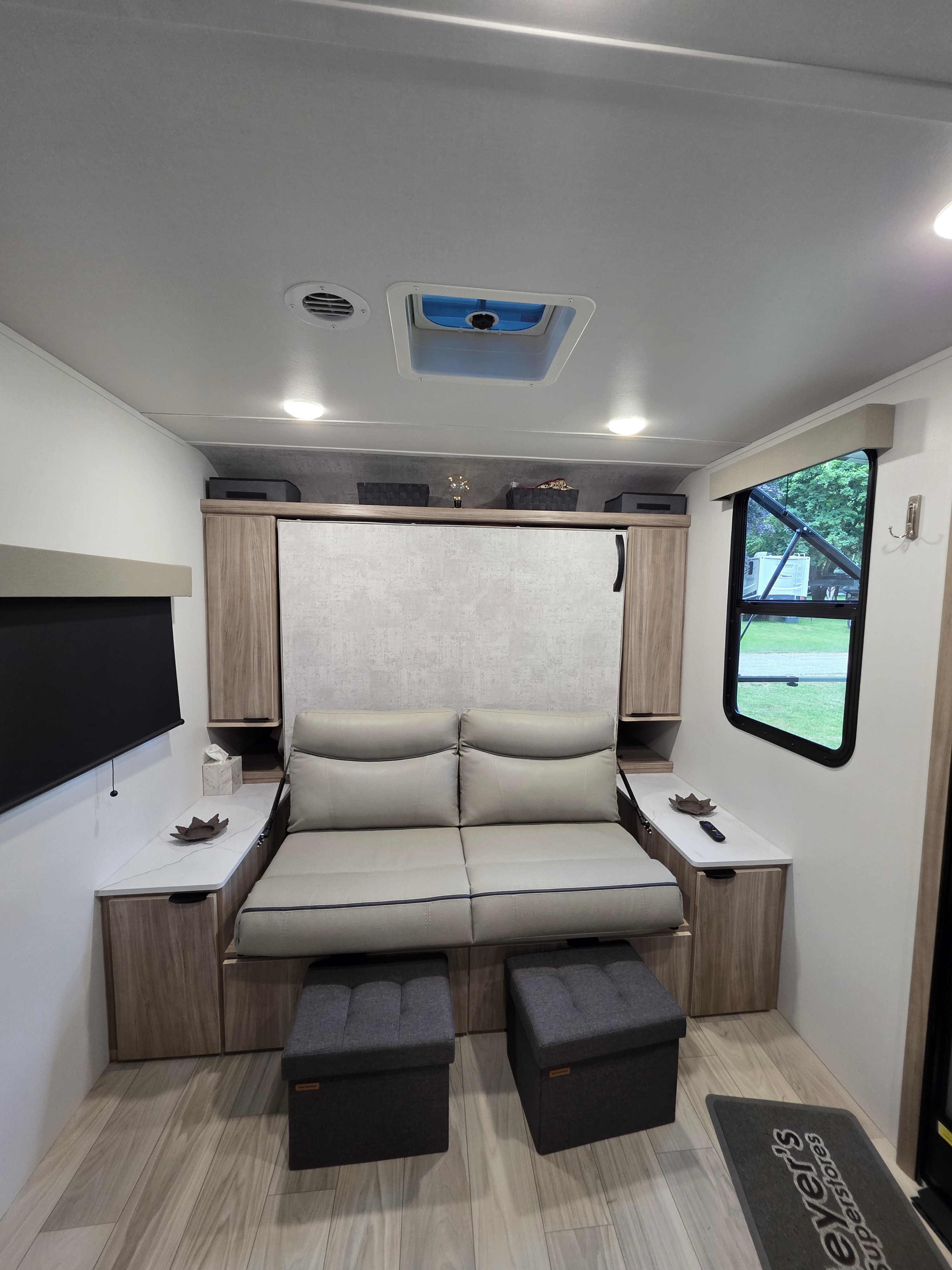 Modern RV rental interior with a light sofa, dark ottomans, TV, and window views, maximizing compact living space.. Winnebago M- Series 2326MBBH 2025