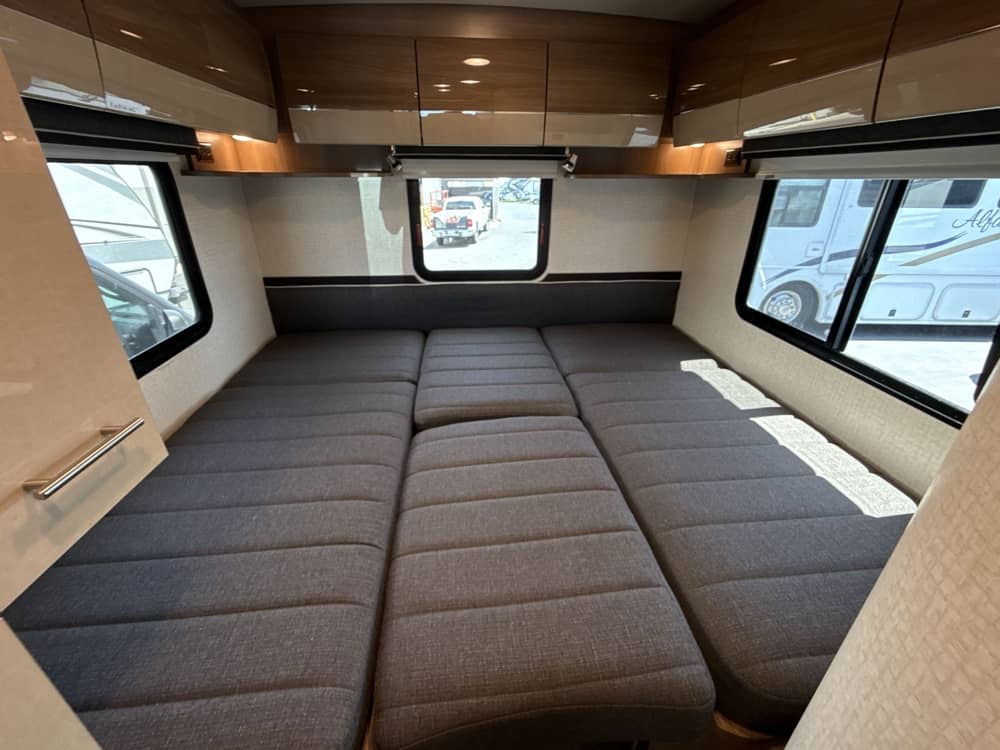 RV rental showing a versatile sleeping area: grey upholstered beds, overhead cabinets, and windows on both sides.. Itasca Navion 2015