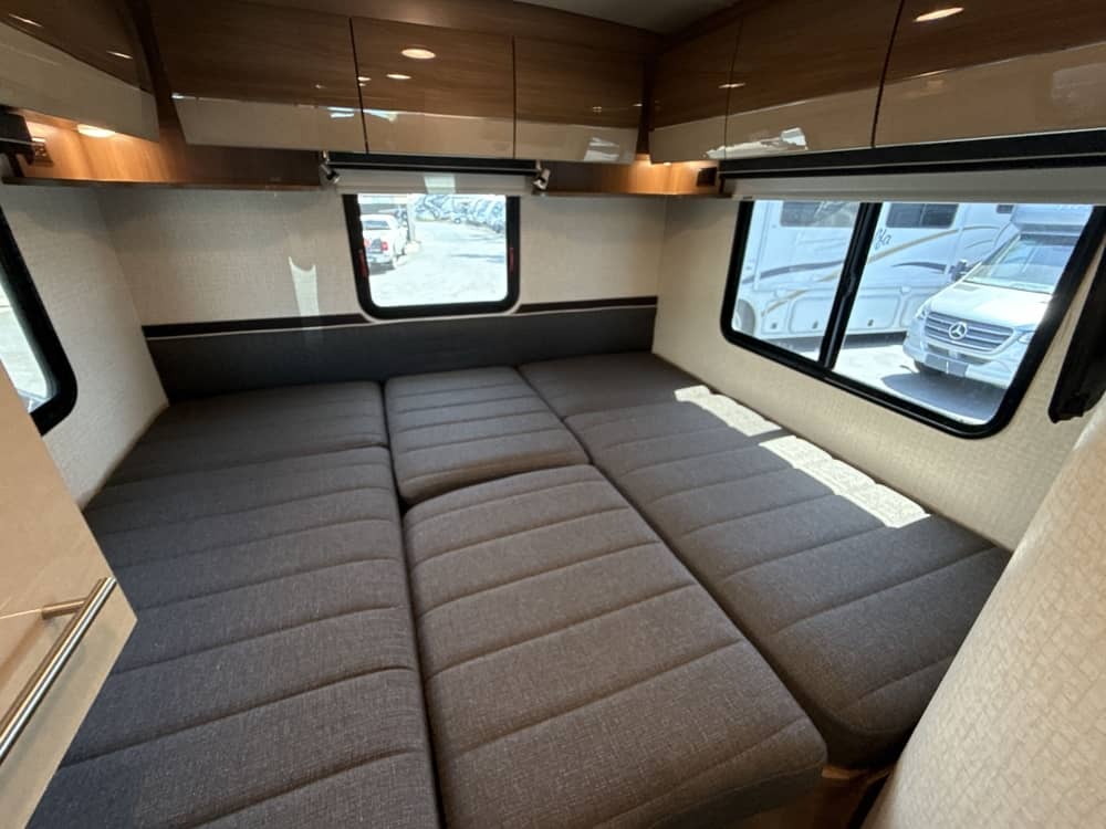 RV rental interior: comfortable grey modular bed/seating area with windows and overhead storage.. Itasca Navion 2015