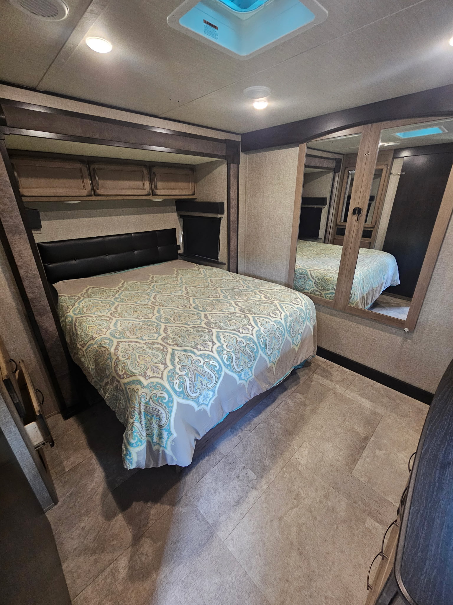 Comfortable RV rental bedroom with patterned comforter, overhead storage, and mirrored wardrobe. Perfect for travel.. Grand Design Transcend 2020