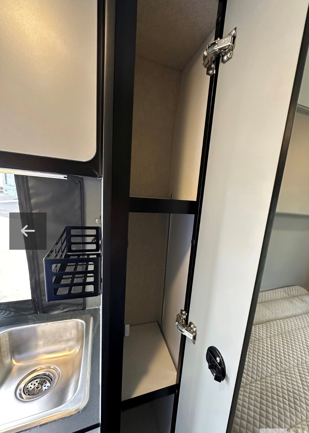 Explore this RV rental's interior: stainless steel sink, hanging basket, and a tall open cabinet with shelves next to a bed.. Winnebago Revel 2025