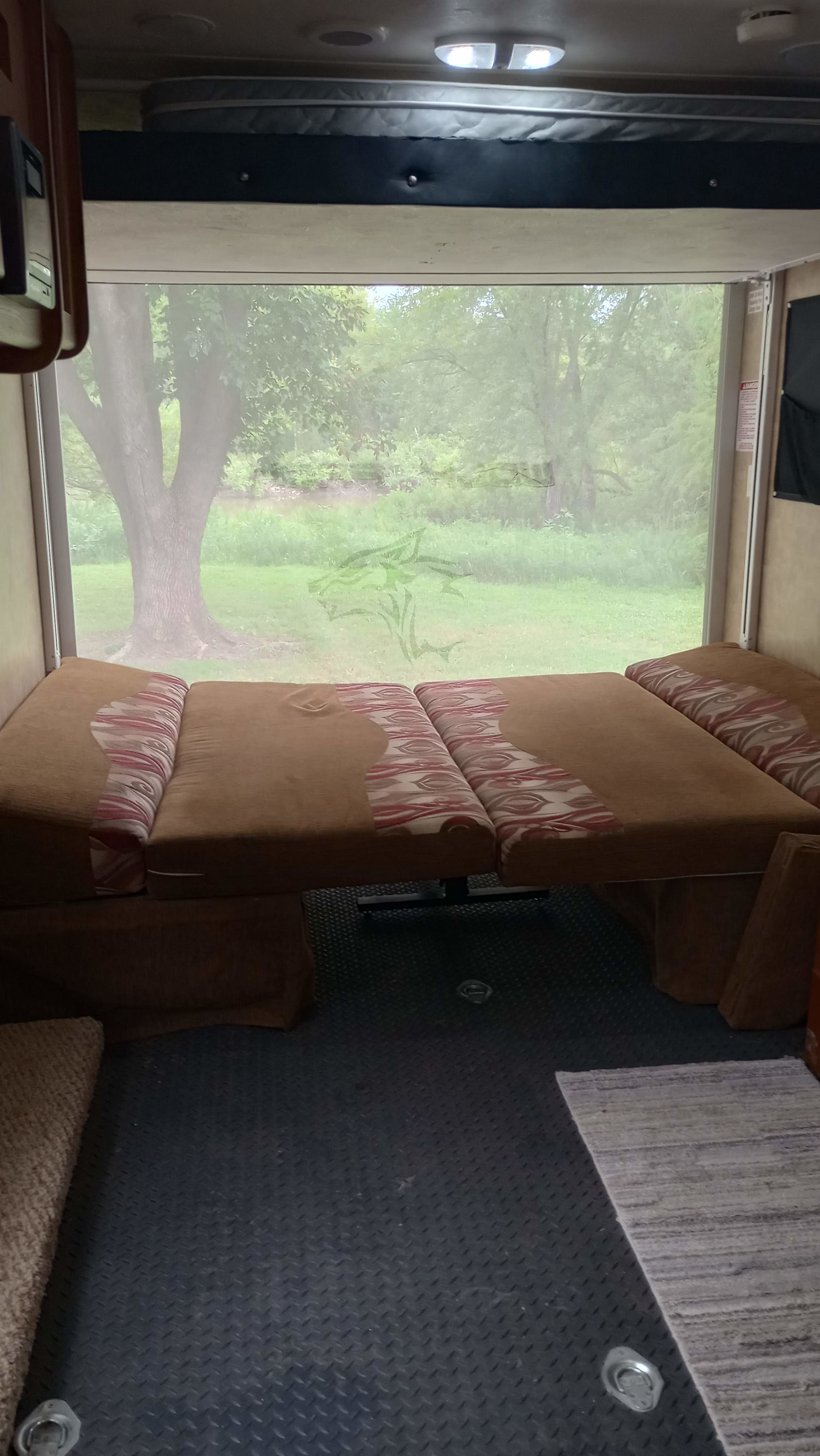 This RV rental interior features a modular sofa/bed, overhead bunk, and expansive rear window overlooking trees and a river.. Forest River Cherokee Wolf Pack 2011
