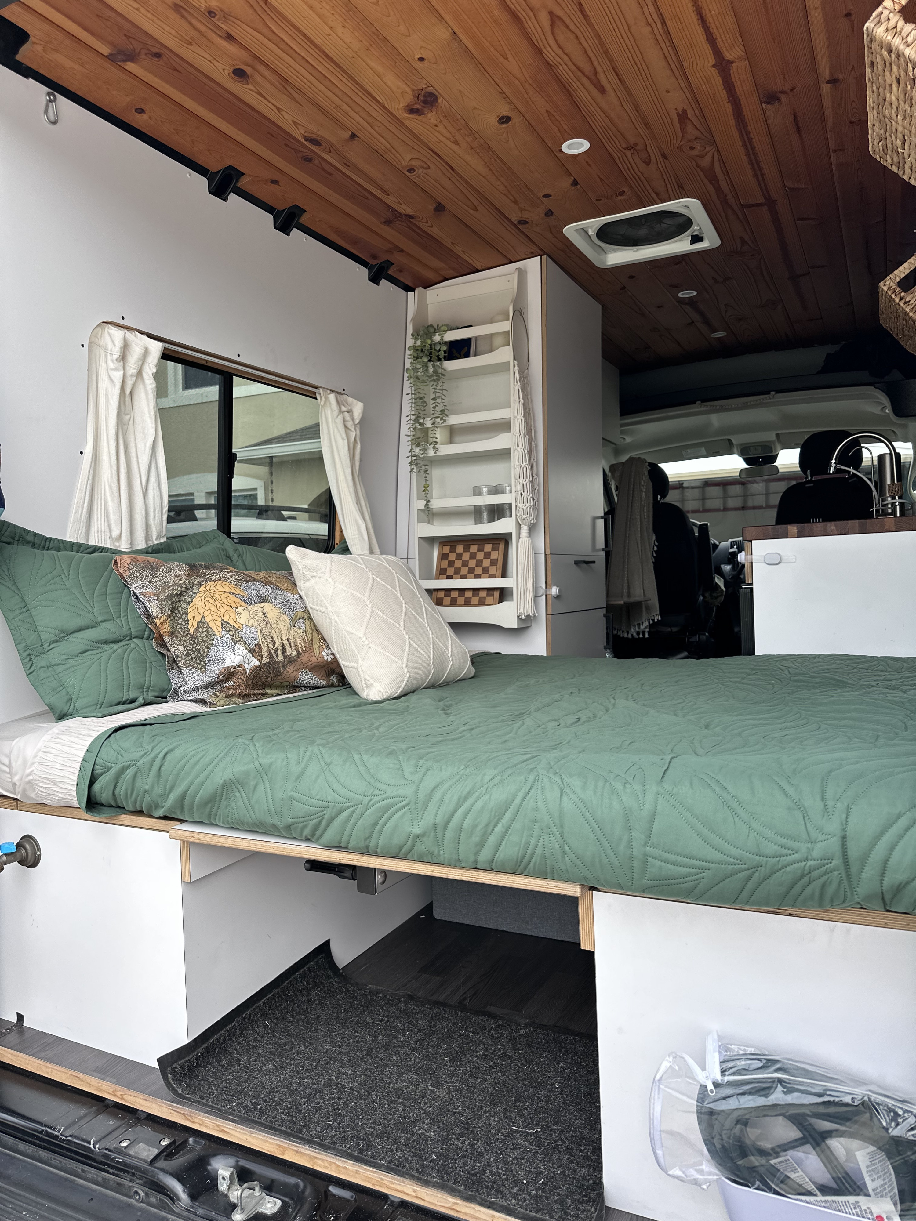 A comfortable RV rental interior with a green quilted bed, warm wood ceiling, and clever built-in storage for travel.. Dodge Sprinter Van 2019