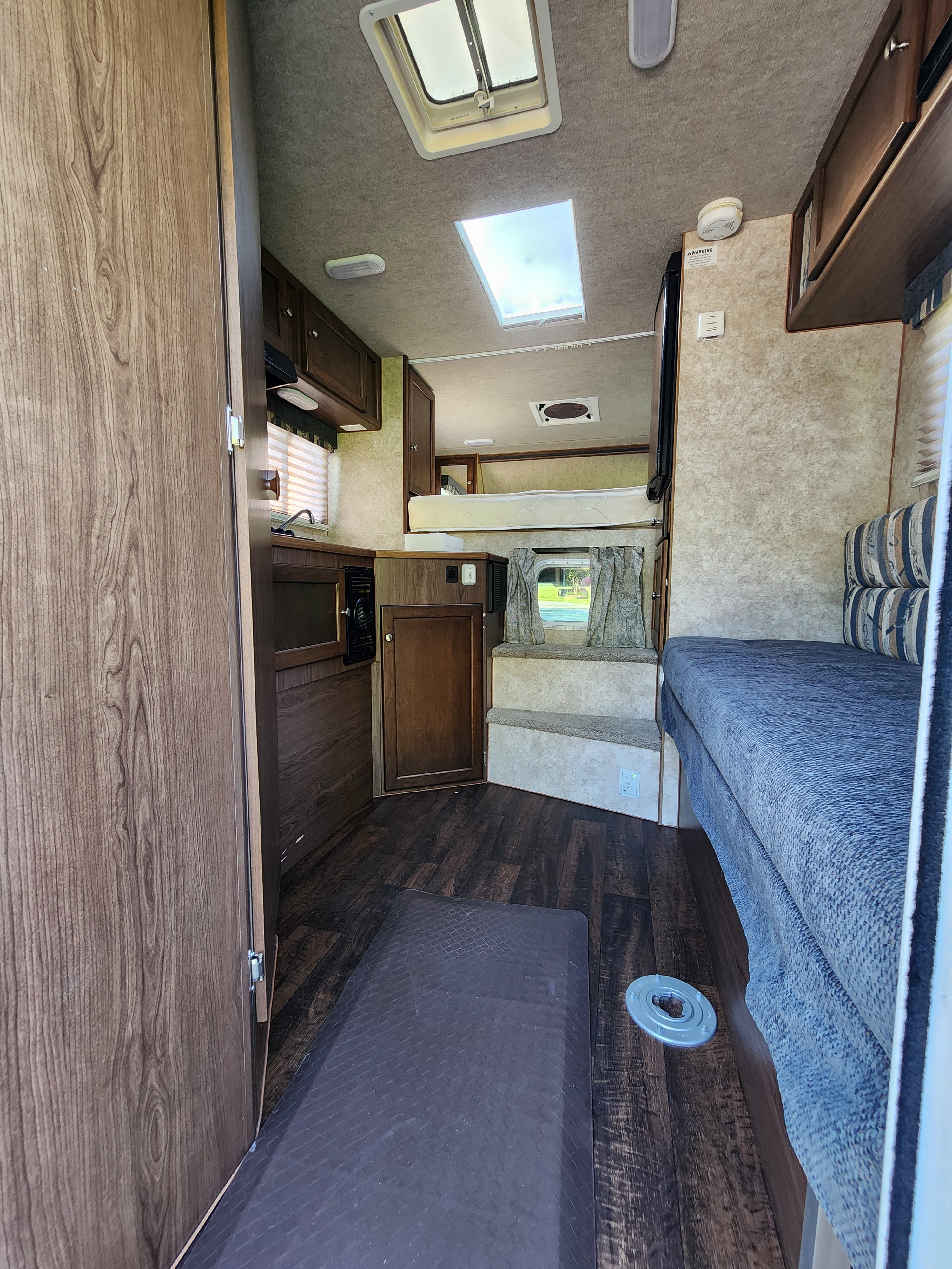 RV rental interior showcasing kitchen (left), overhead bed, and living area with steps leading to a windowed lounge.. Ford Ford F150 2017