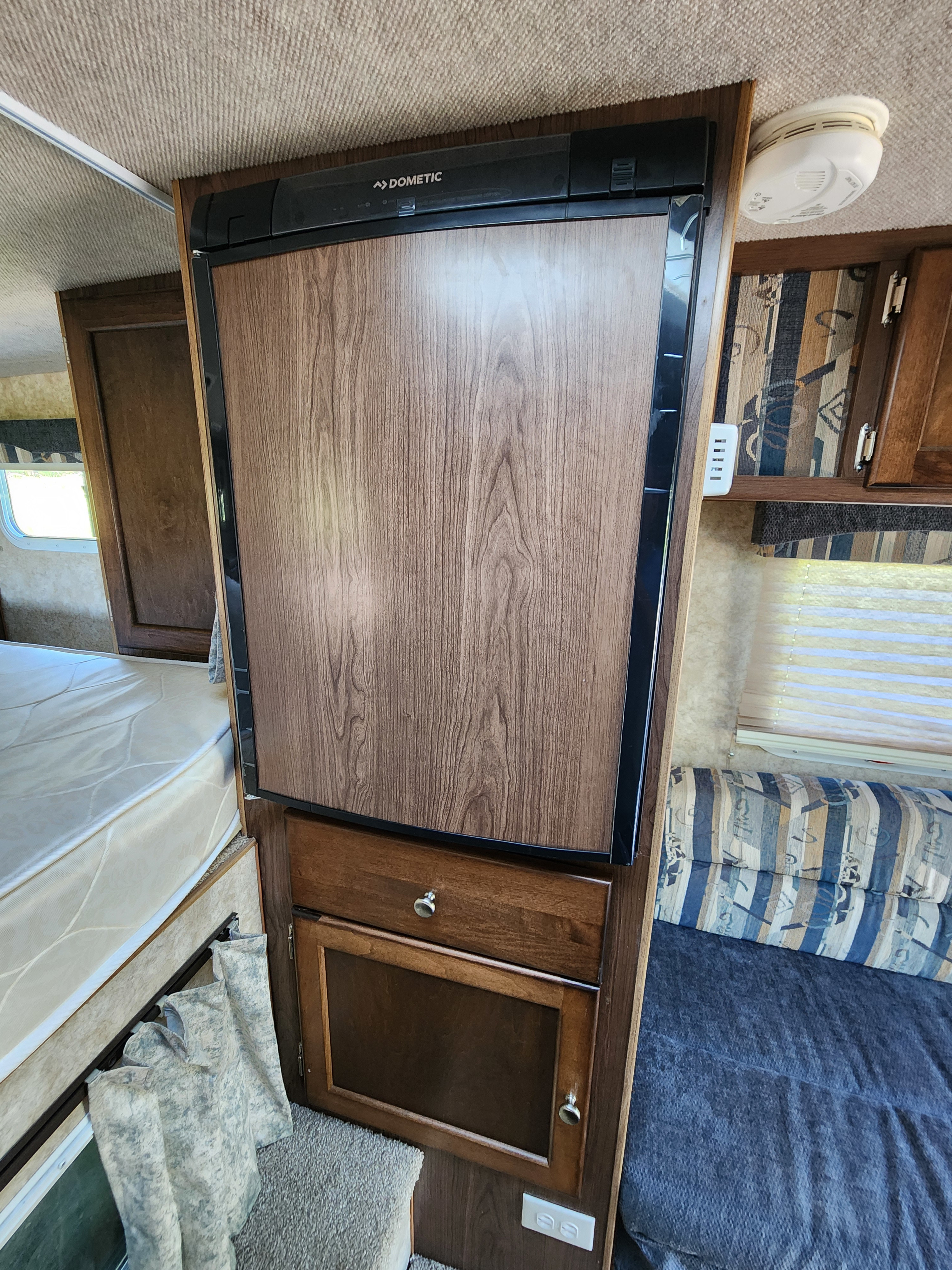 Interior of an RV rental, showcasing a Dometic refrigerator, sleeping area, striped seating, and wood cabinets for storage.. Ford Ford F150 2017