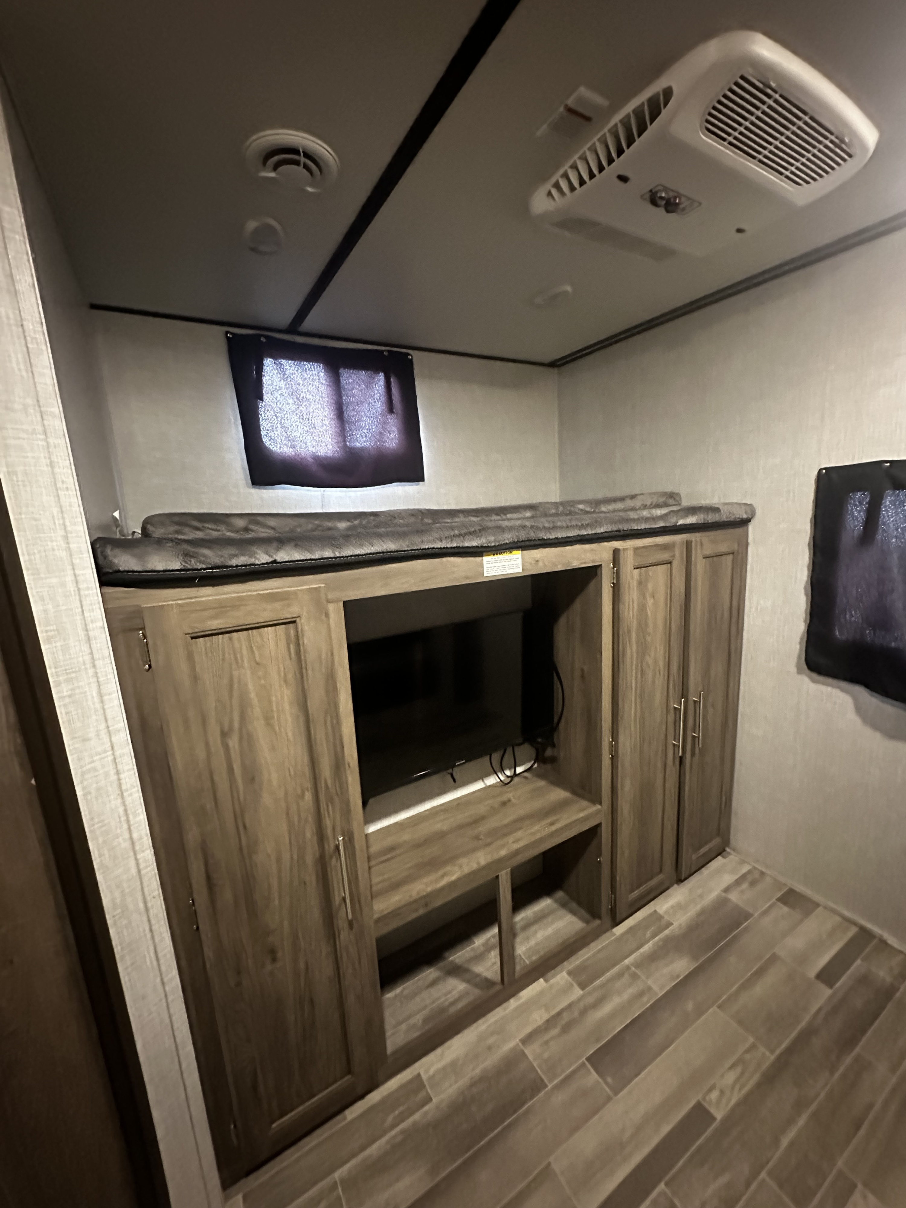 RV rental interior: bunk beds over a TV entertainment unit with storage, featuring a ceiling AC unit and wood-look plank flooring.. Crossroads RV Zinger 2020