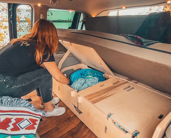 Inside an RV rental, a person organizes clothes in custom wood storage. Ideal for a tidy camper van adventure.. Dodge B Van 2014