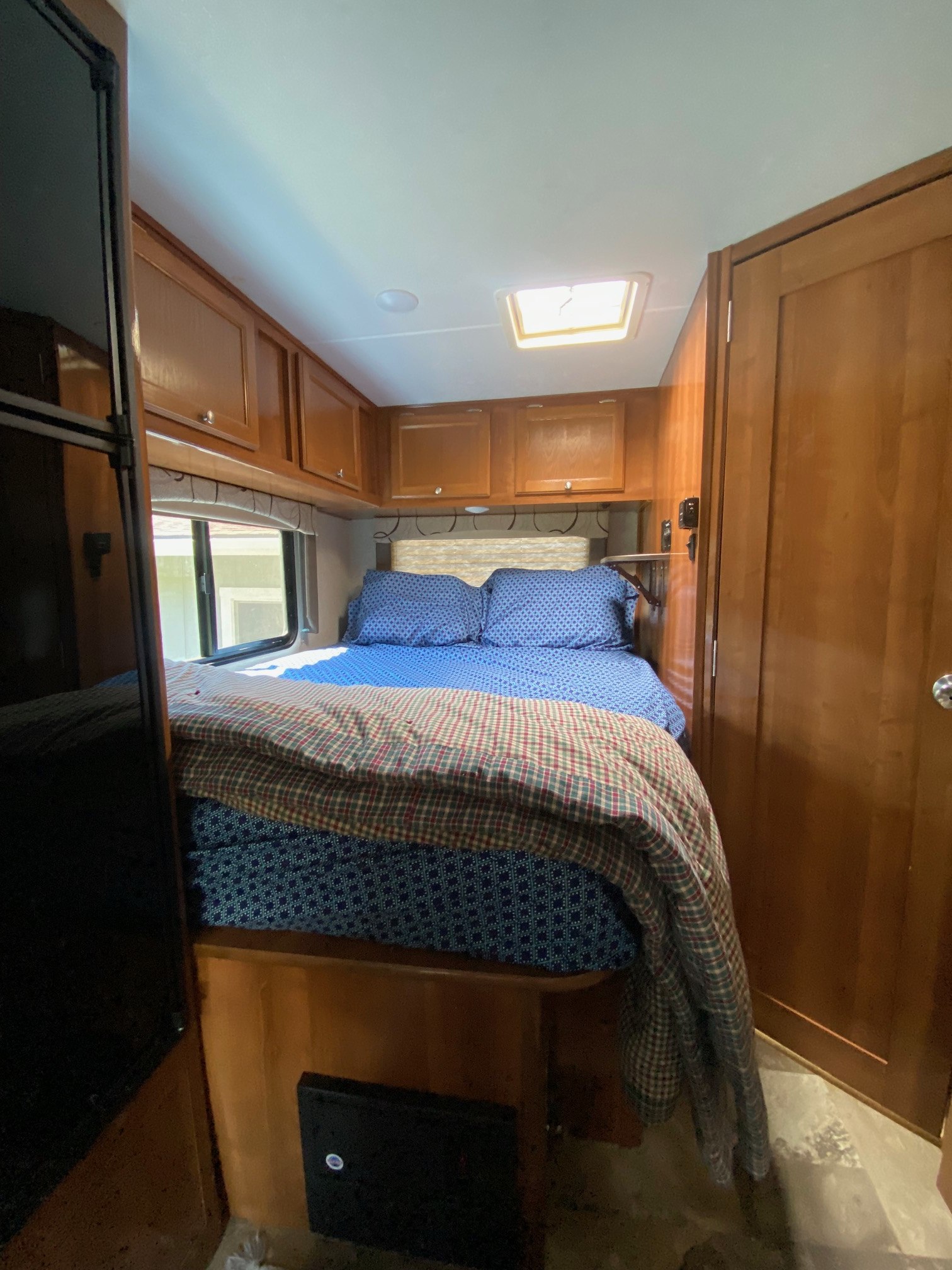 RV rental bedroom interior, featuring a bed with patterned linens, wood cabinets, window, and skylight.. Forest River Coachmen Leprechaun 2019
