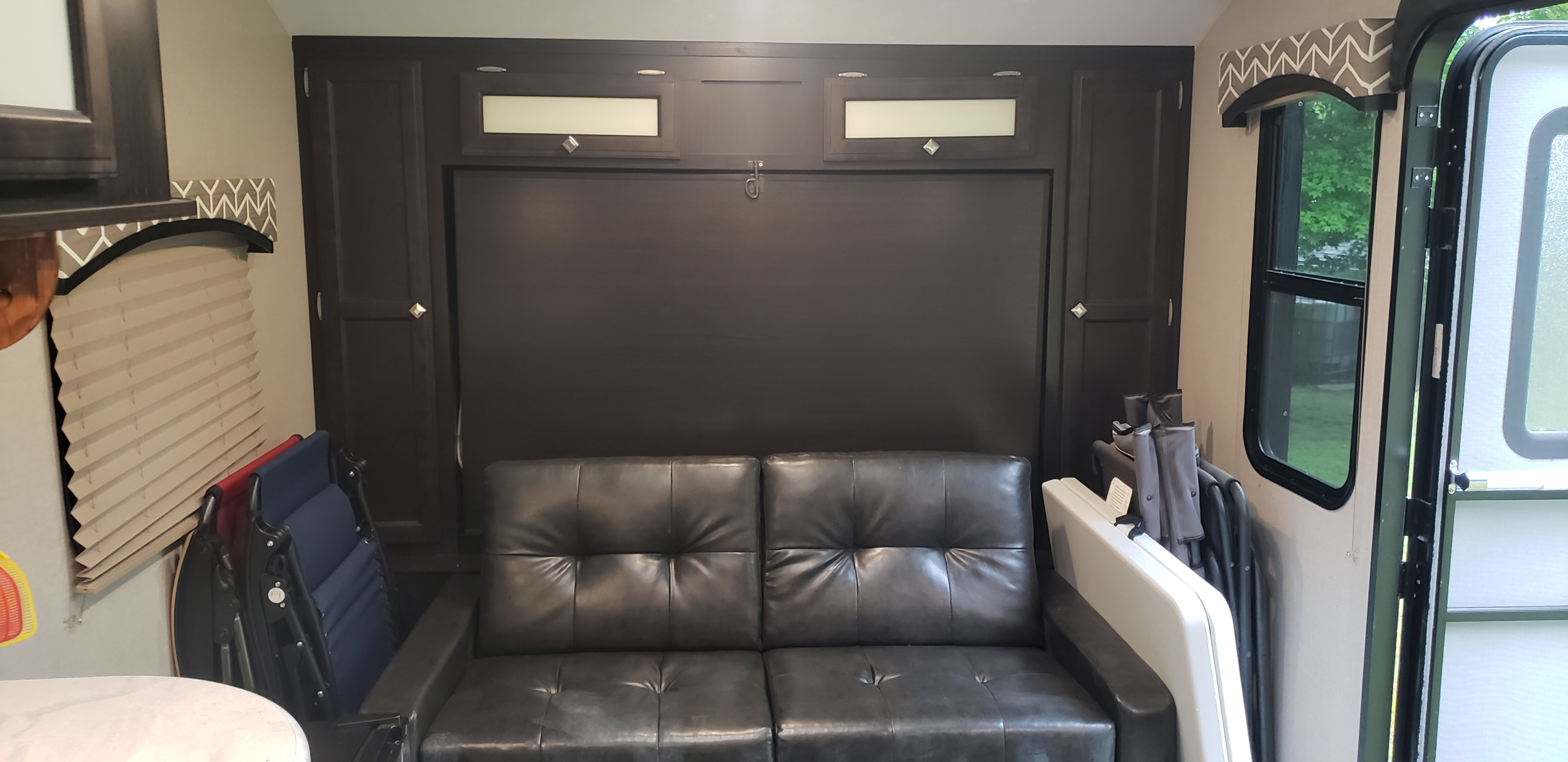 Spacious RV rental interior featuring a dark sofa that converts to a murphy bed, with ample overhead storage and a bright window.. Sonic Sonic Trailer 2018