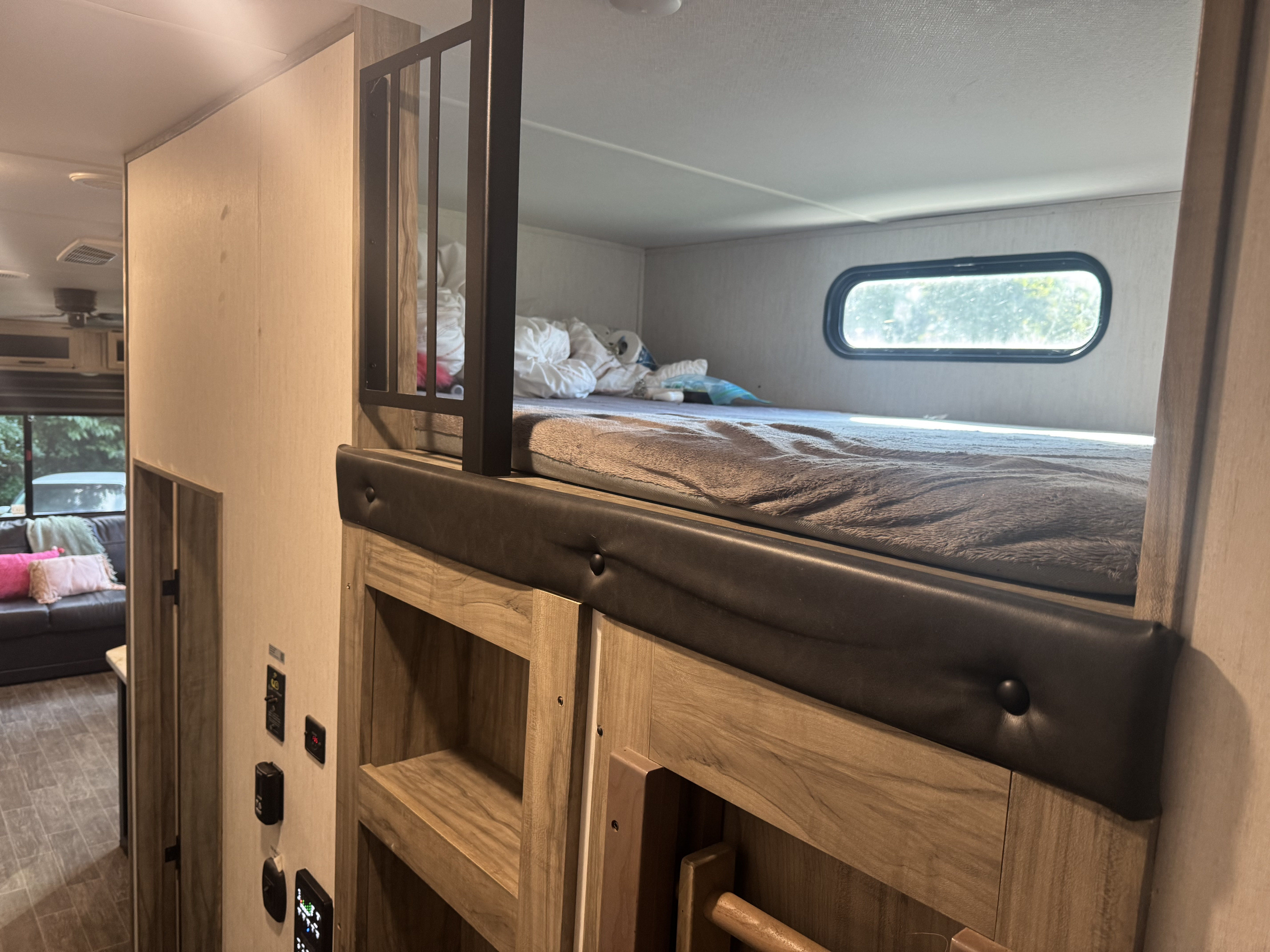 Inside an RV rental, a cozy bunk bed with a window and built-in shelves. A living area with a couch is visible beyond.. Arctic Fox 3660 Suite 2023