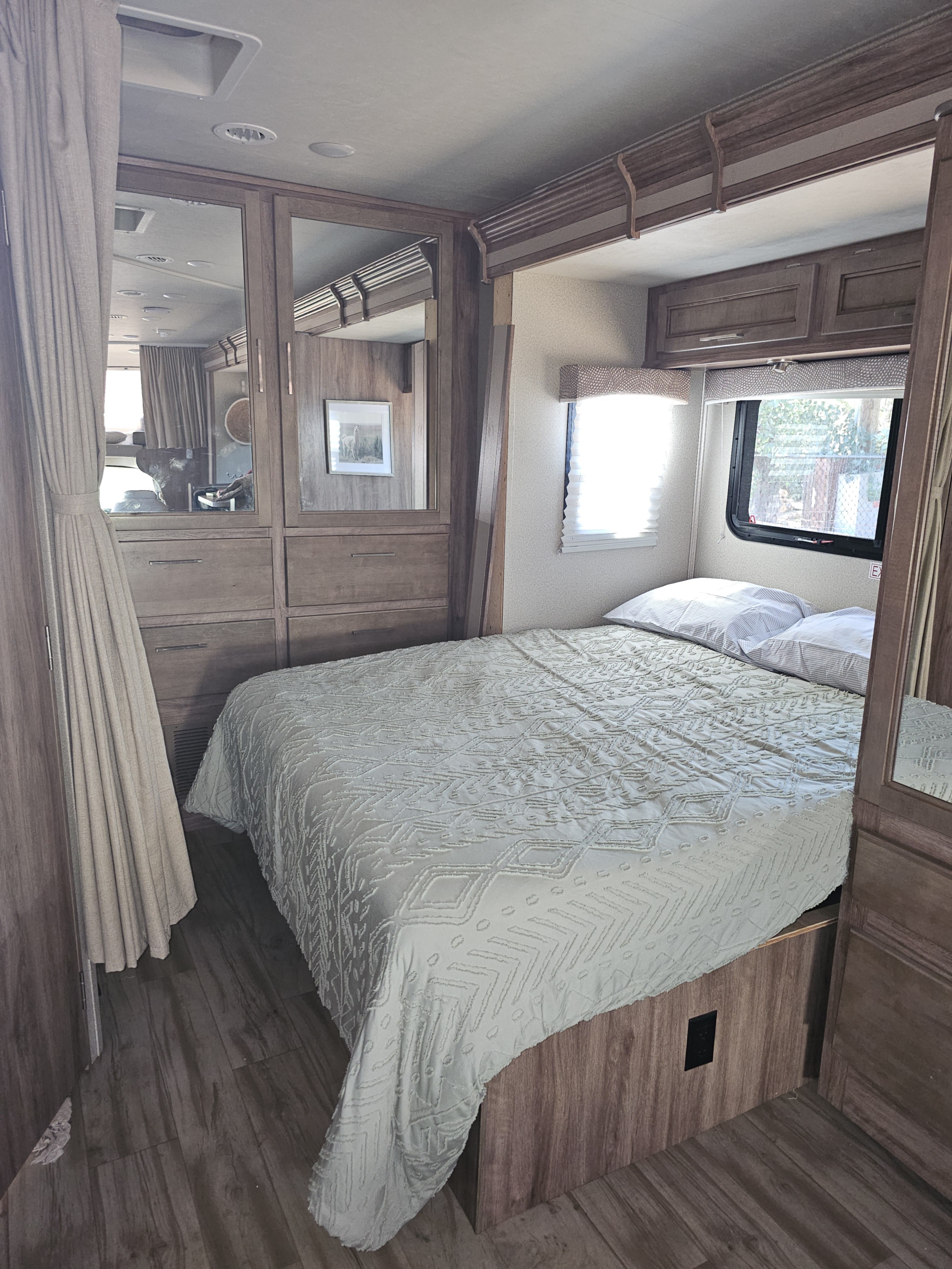 Spacious RV rental bedroom featuring a comfortable bed, wood-look cabinets, and bright windows. Ideal travel accommodation.. Entegra Coach Odyssey 2019