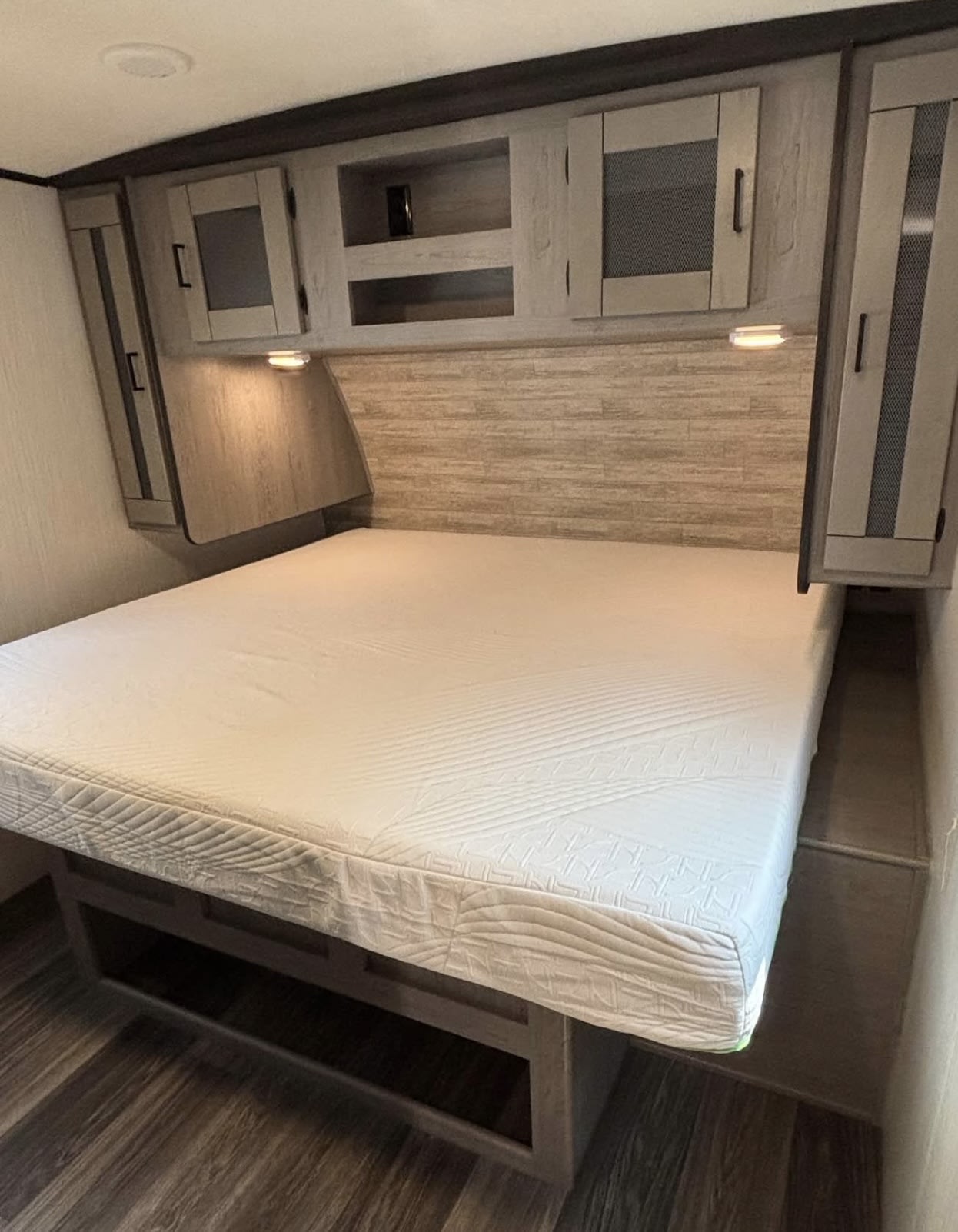 Experience comfort in this RV rental bedroom: bed with storage, overhead cabinets, reading lights, and wood-look decor.. Heartland RVs Mallard 2021