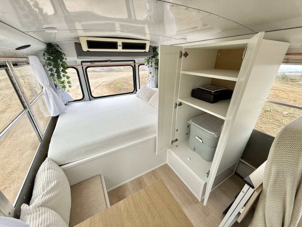 Cozy RV rental bedroom with white bed, storage cabinet showing a portable toilet, and windows overlooking a desert landscape.. Chevrolet Express G3500 2007