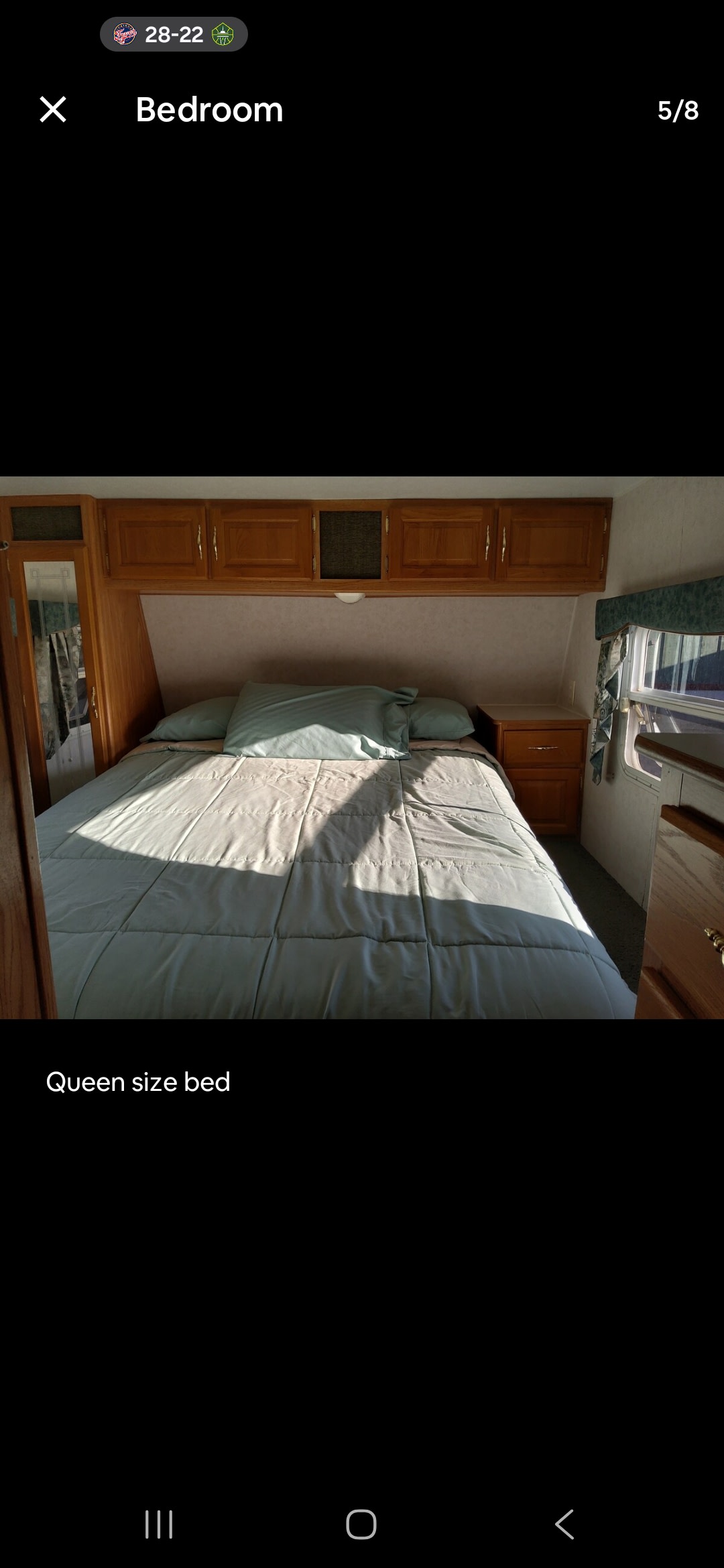 Cozy RV rental bedroom with a queen size bed, overhead wooden cabinets, and window. Sunlight casts shadows on the bed.. Dutchmen TL 2000