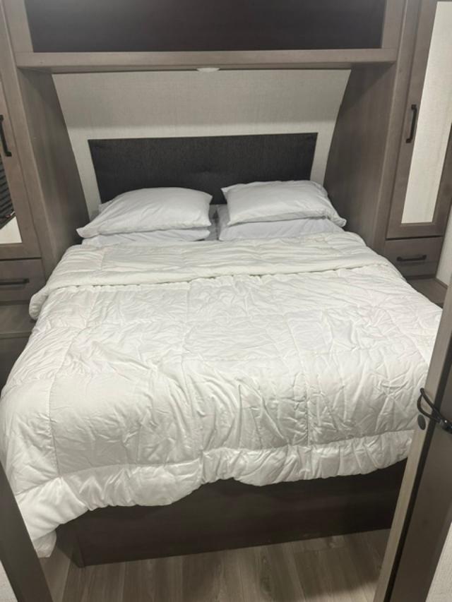 Interior of an RV rental: a clean queen bed with white bedding, surrounded by built-in storage for a comfortable stay.. Grand Design Transcend Xplor 2024