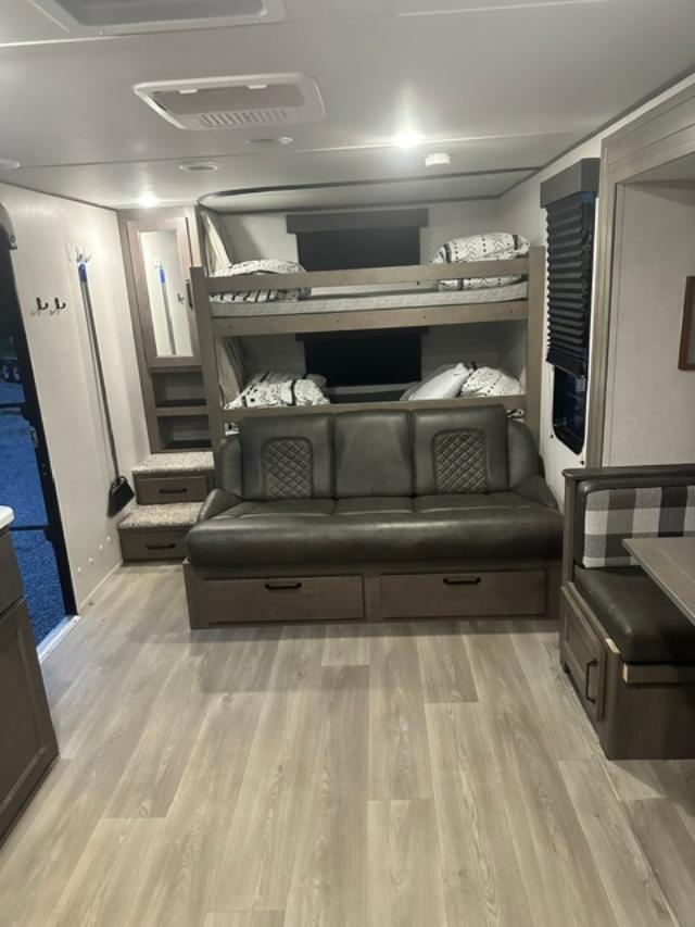 RV rental interior: bunk beds, a dark sofa with storage drawers, and a dinette with plaid cushions on light flooring.. Grand Design Transcend Xplor 2024
