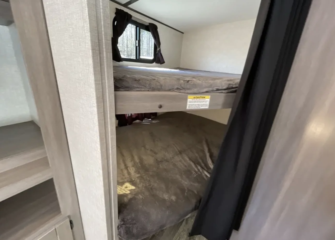 RV rental bunk beds provide a compact sleeping area with upper and lower bunks, visible with grey bedding, ideal for travel trailer trips.. Keystone RV Sunset Trail 242BH 2022