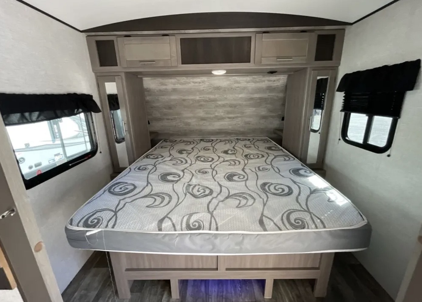Experience comfort in this RV rental bedroom featuring a full bed, overhead storage, and large windows.. Keystone RV Sunset Trail 242BH 2022