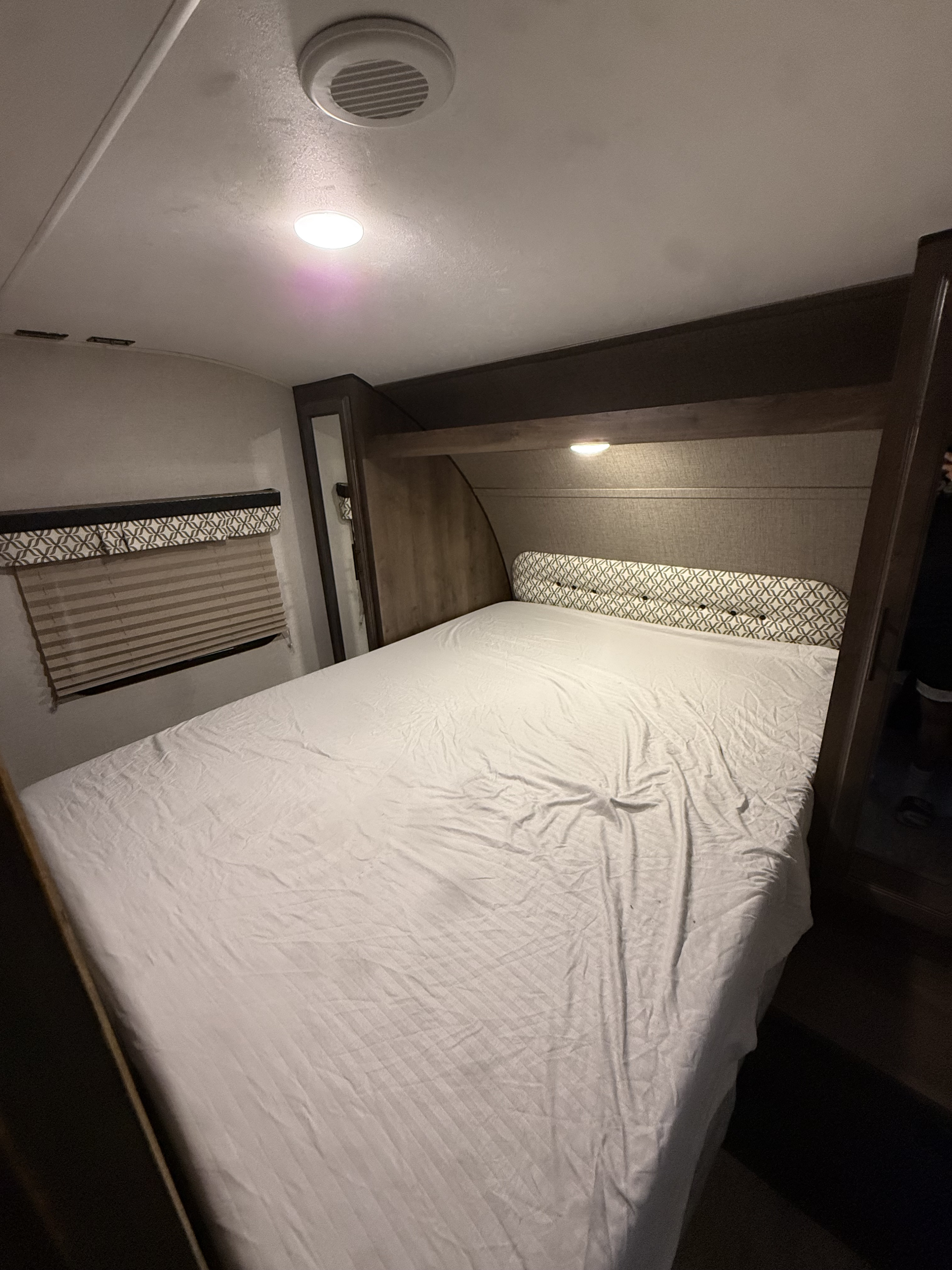 Cozy RV rental bedroom featuring a large bed with white, striped sheets, patterned headboard, and window with blinds.. KZ connect 241 bhk 2019