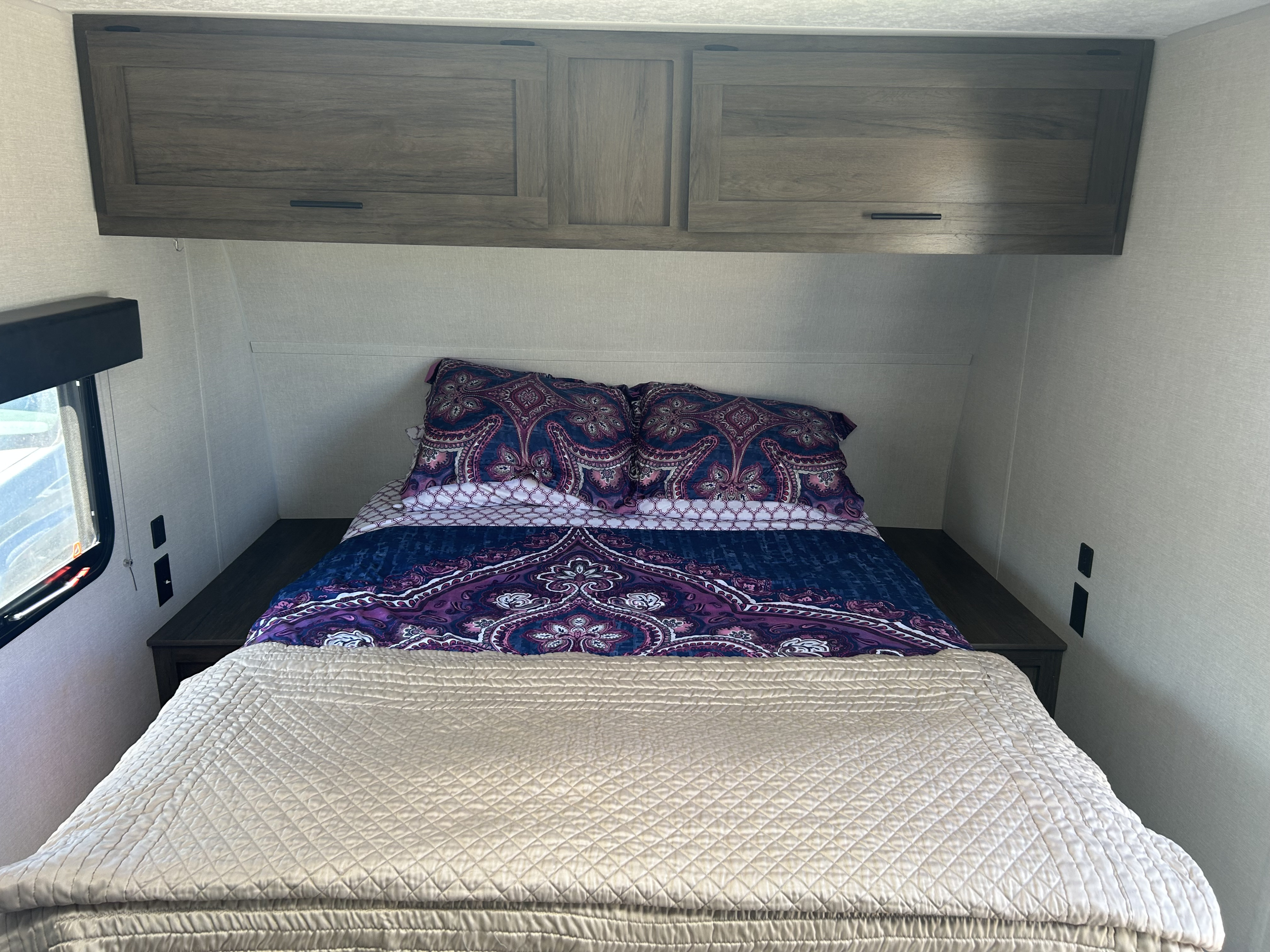 Inside an RV rental: a neat bedroom with vibrant paisley bedding, practical overhead storage, and bedside charging.. Avenger LT 2021