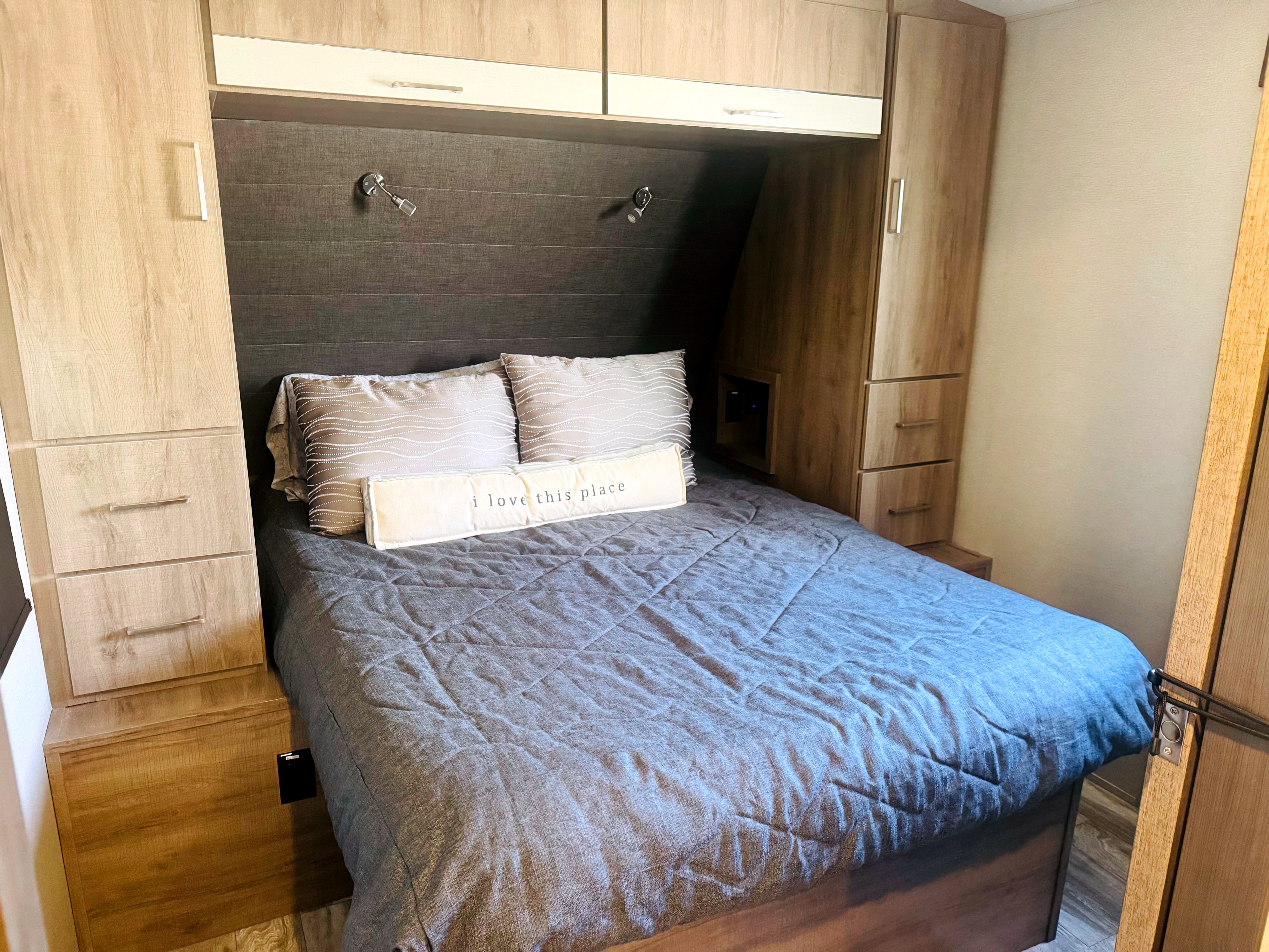Cozy RV rental bedroom featuring a comfy bed, overhead storage, and reading lights, perfect for your next road trip adventure.. Grand Design Imagine 2022