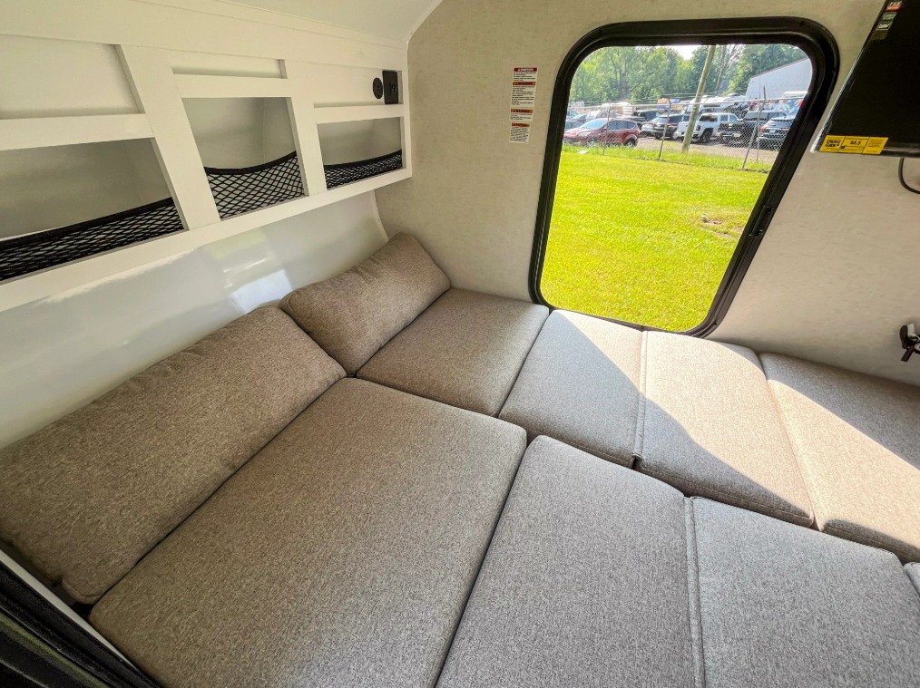 Cozy RV rental interior with convertible bed/seating, storage shelves, and window view.. Modbug 10RK 2025