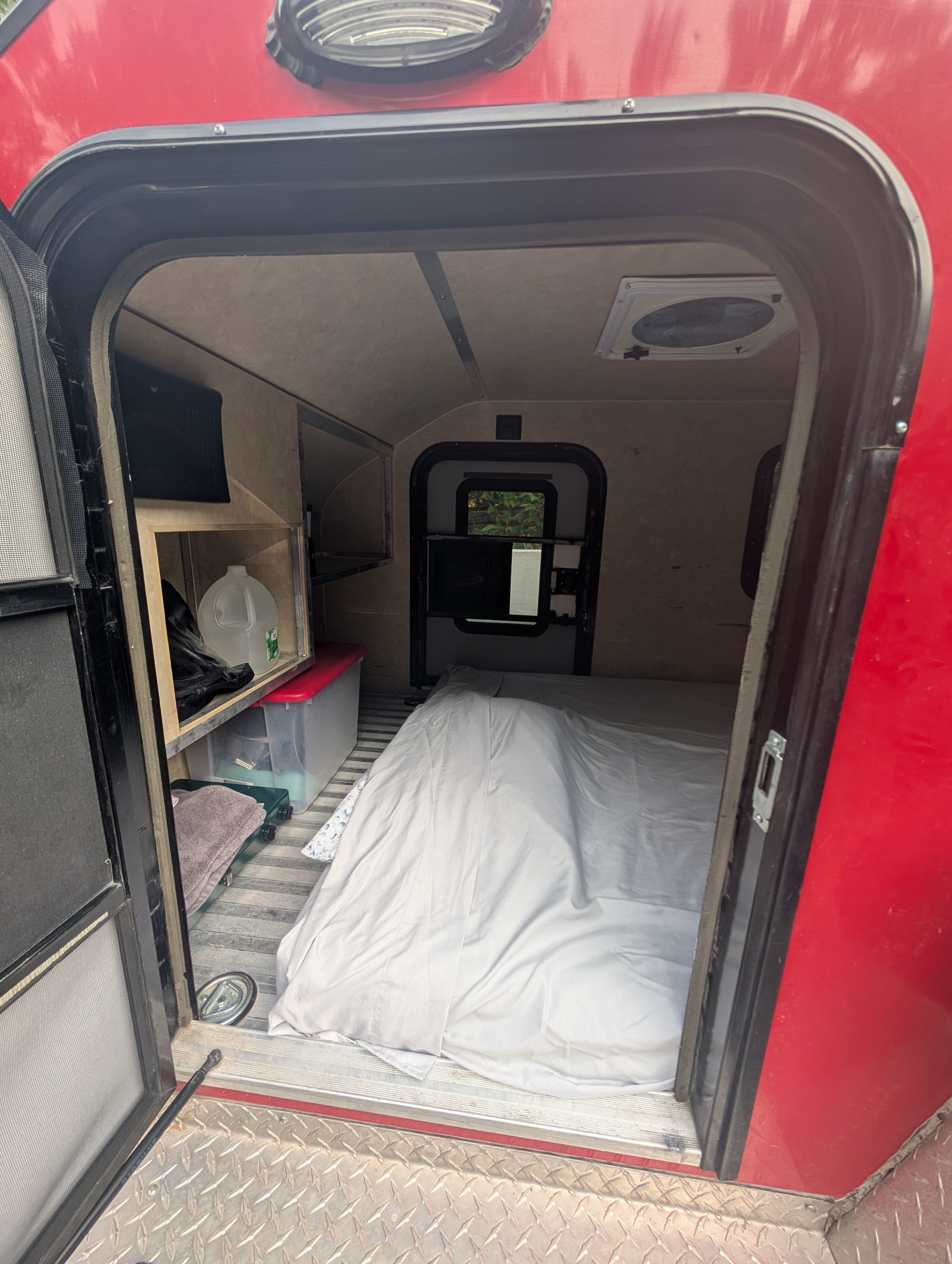 Inside a cozy RV rental: bed, storage shelves, and vent visible from the open doorway. Perfect for adventurers.. Micro-lite Cargolite 2016