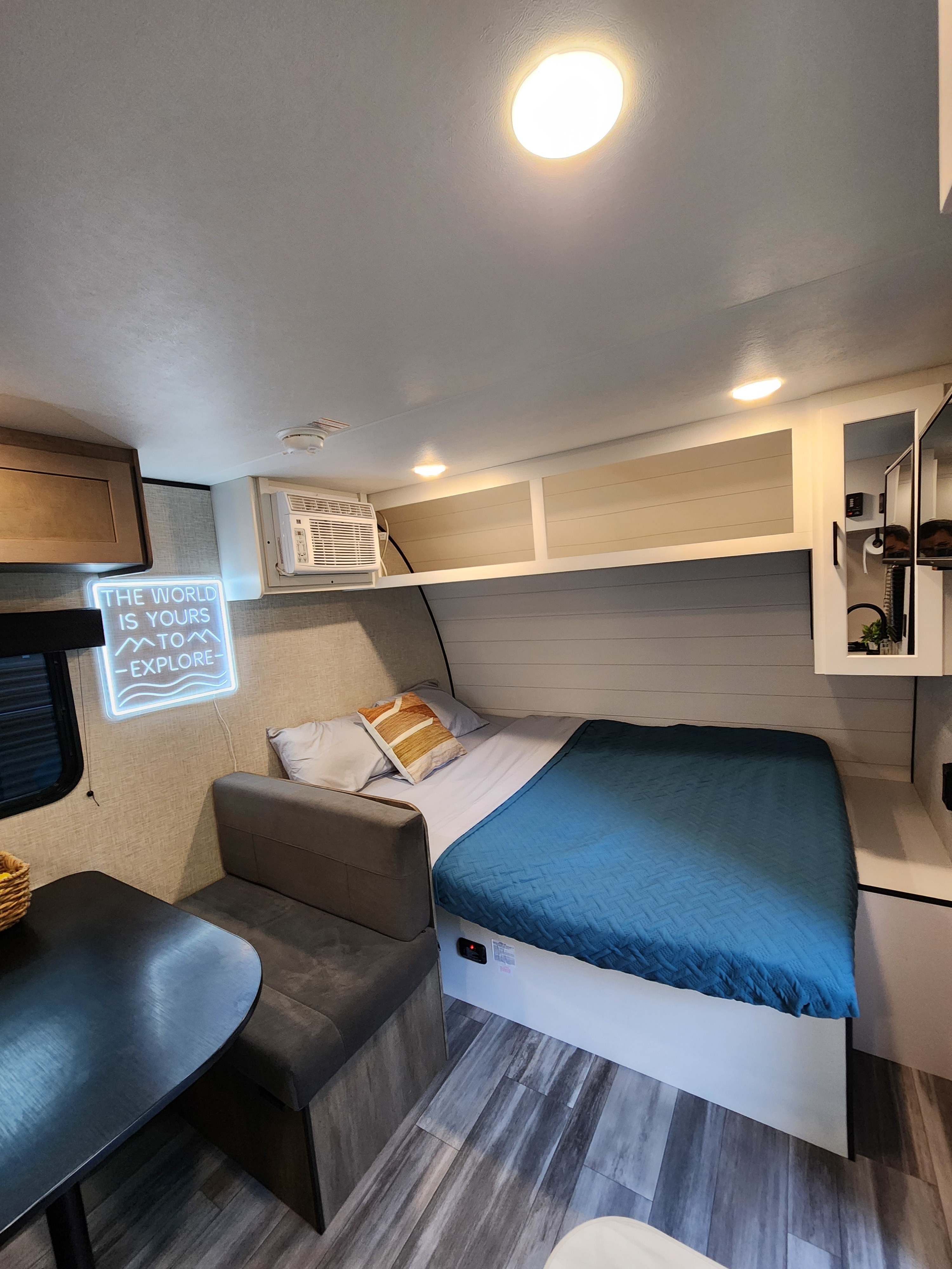 Step into this inviting RV rental interior: comfortable bed, dinette, AC, and an "explore" neon sign.. Jayco Jay Flight SLX 2024