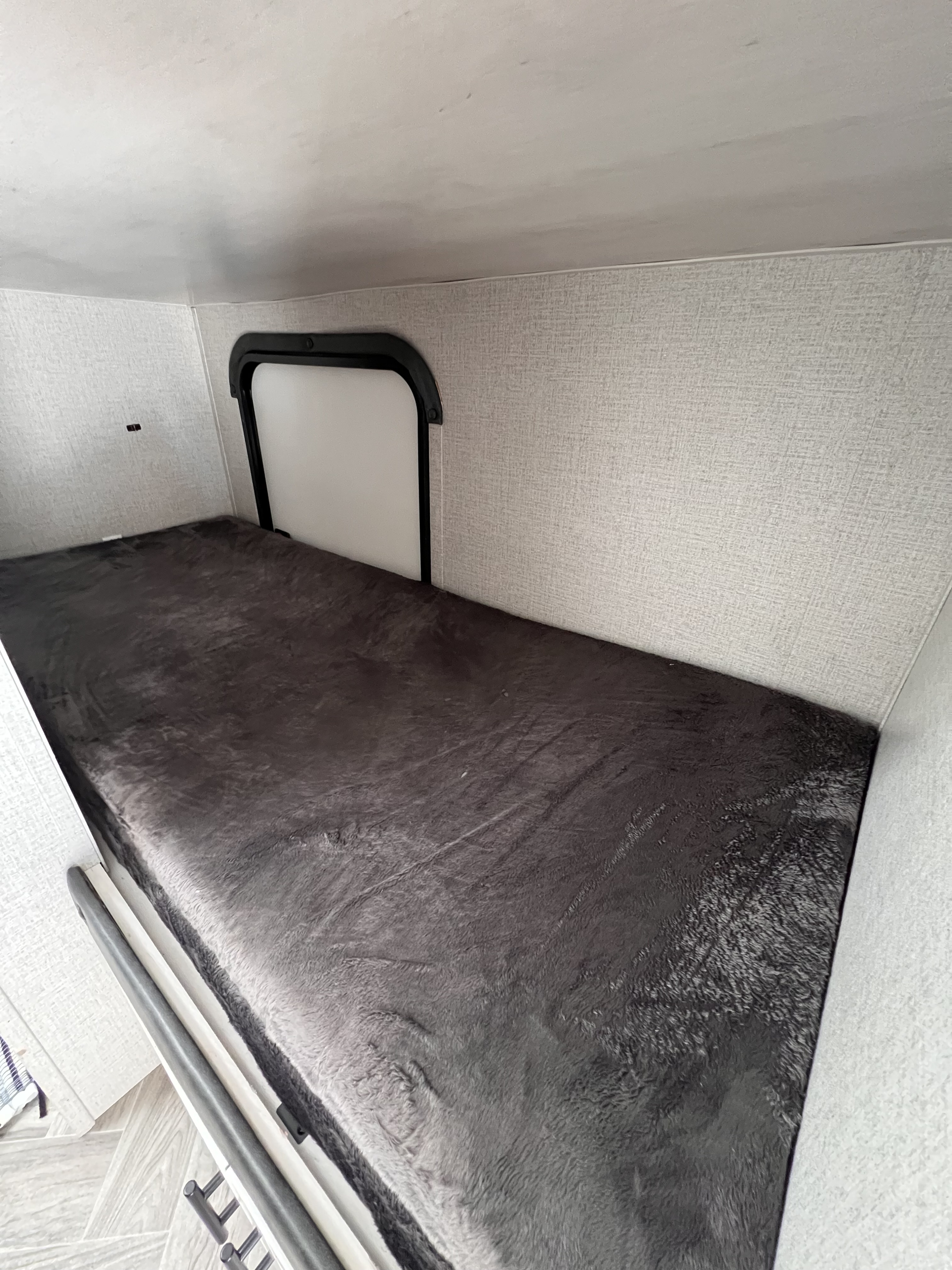 Inside an **rv rental**: a comfortable bunk bed with soft dark bedding and a window for light, ideal for travel.. Dutchmen Coleman Rubicon 2021
